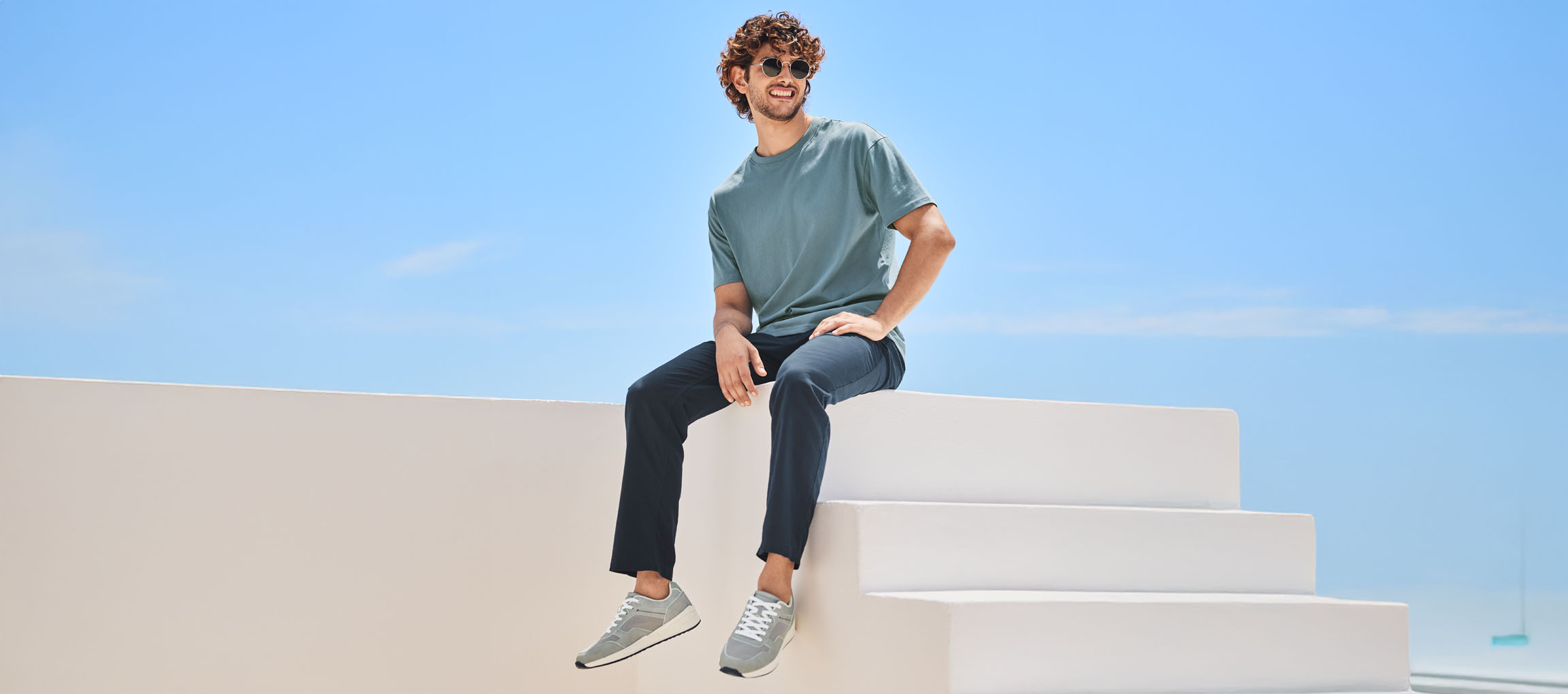 Mees t-särgis, püksides ja New Balance tossudes, istub valgetel treppidel.
