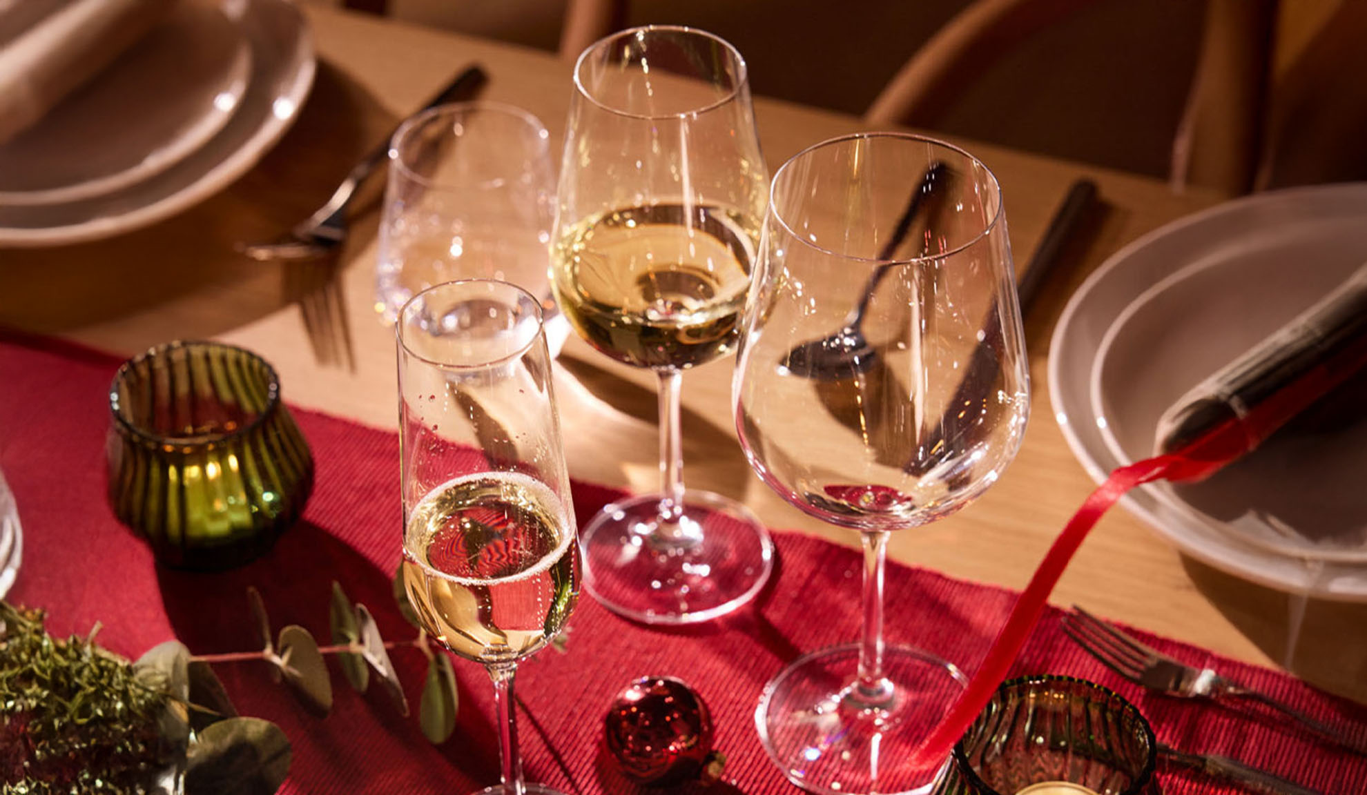 Празднично накрытый стол с бокалами для вина, бокалом для шампанского и рождественскими украшениями.