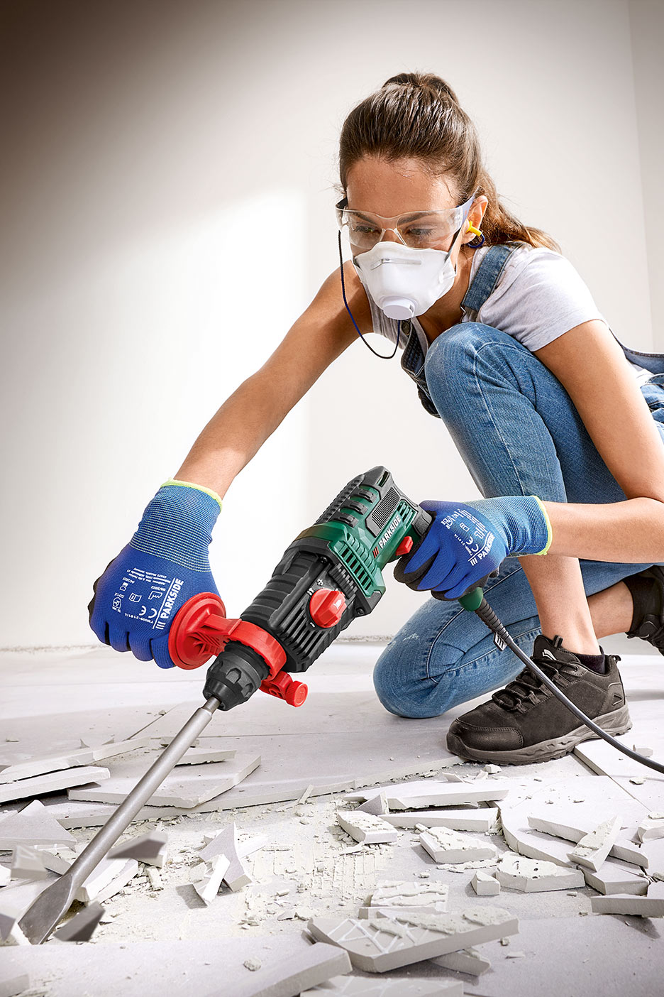 Naine kaitseprillide ja maskiga kasutab plaadi eemaldamiseks piikvasarat.