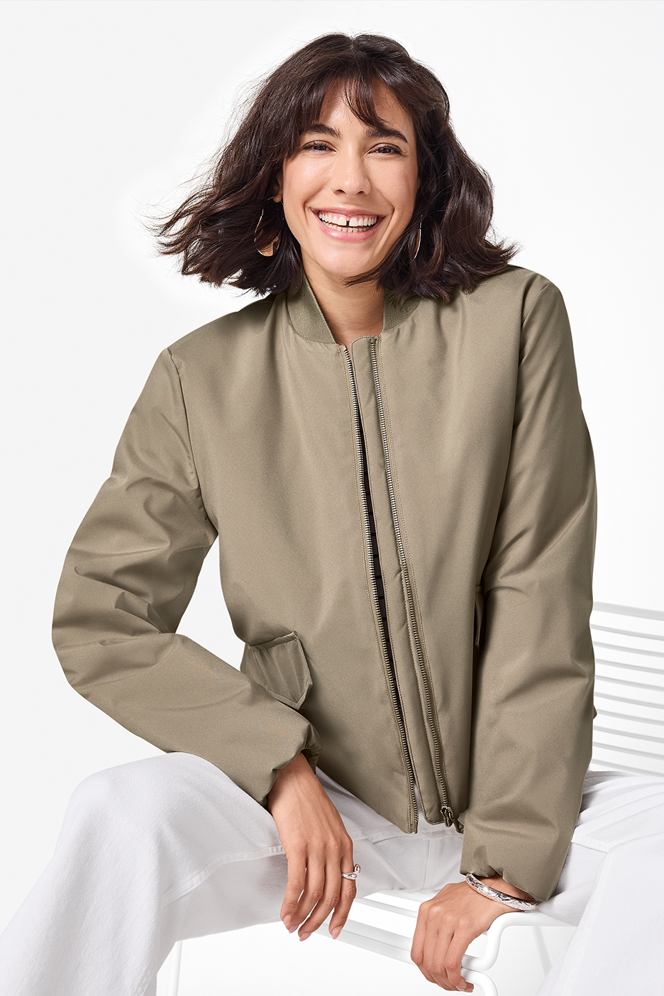 Naine kannab beeži pommitajat ja valgeid pükse, naeratades kaamerasse.