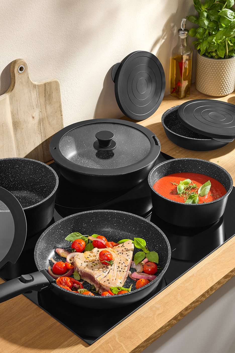 Mustad graniitkattega potid ja pannid induktsioonpliidil, toiduga ja kaantega.