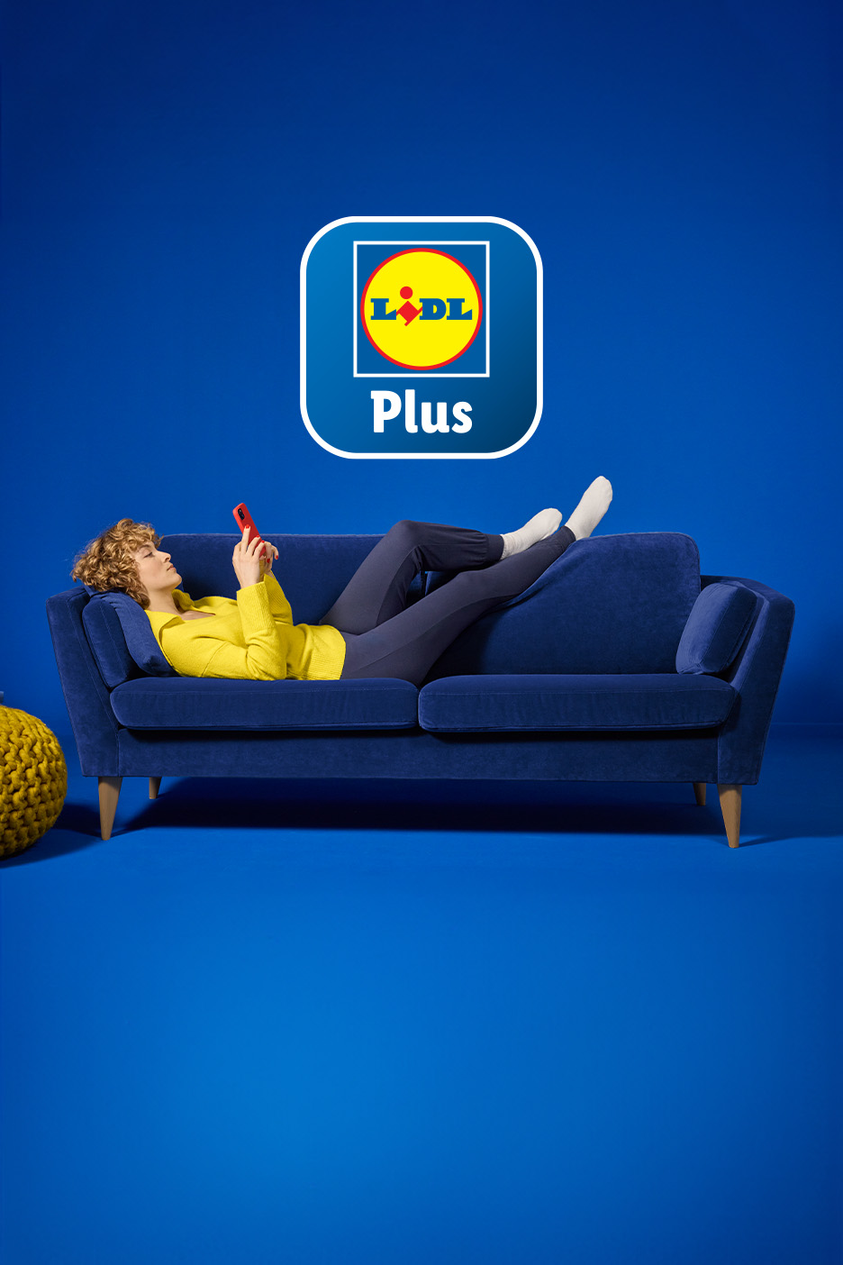 Naine lamab sinisel diivanil, vaatab telefoni, lähedal on Lidl Plusi logo.
