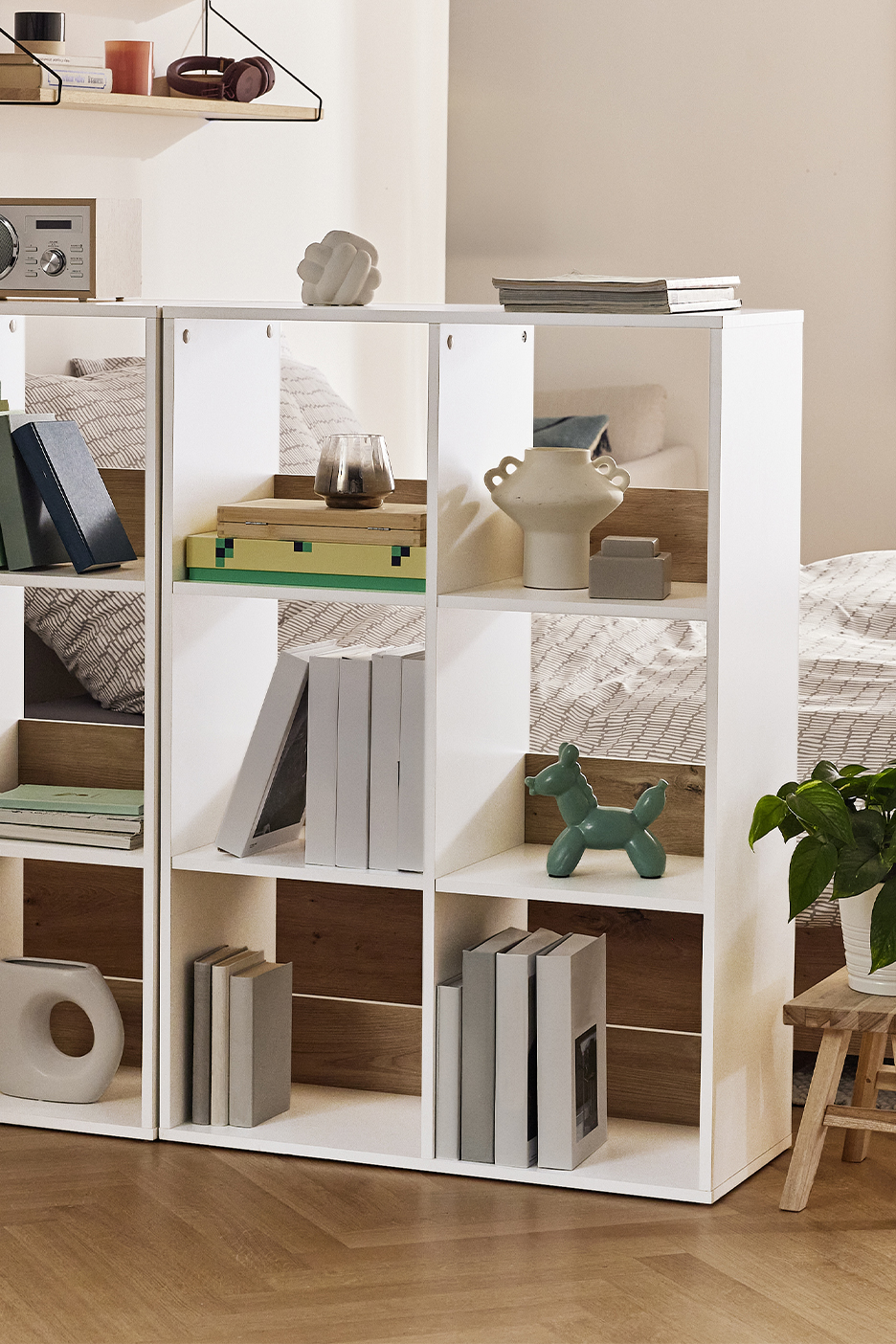 Valge ruumijagaja riiul raamatute, vaaside ja dekoratiivesemetega.