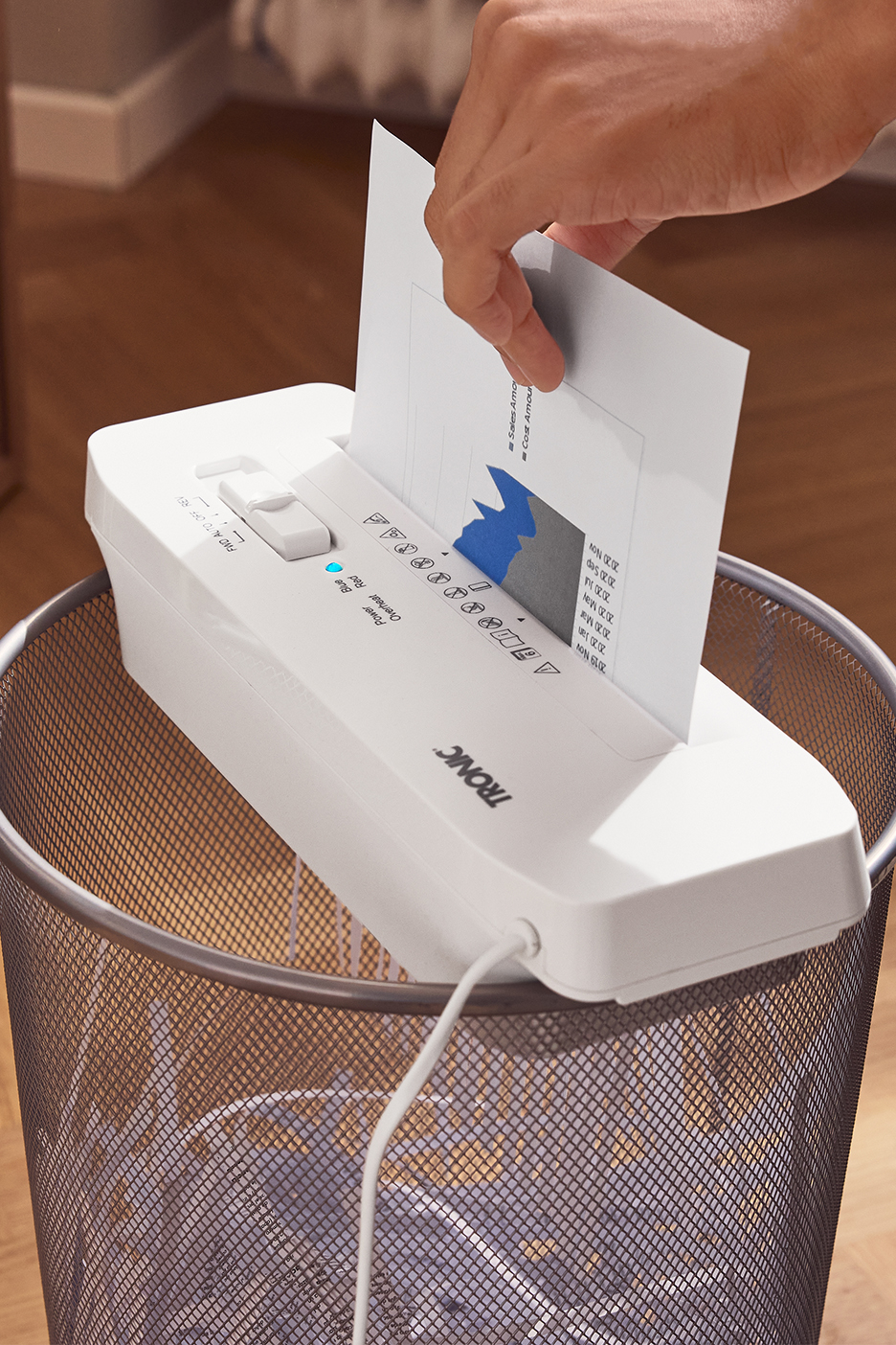 Käsi sisestab dokumendi TRONIC paberipurustajasse, mis on asetatud prügikorvi peale.