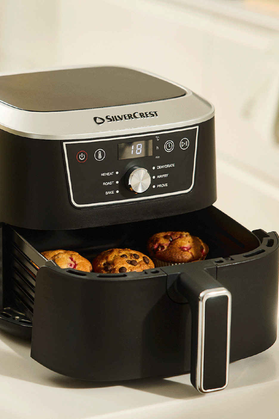 Must õhufritüür koos muffinite, digitaalse ekraani ja juhtnuppudega.