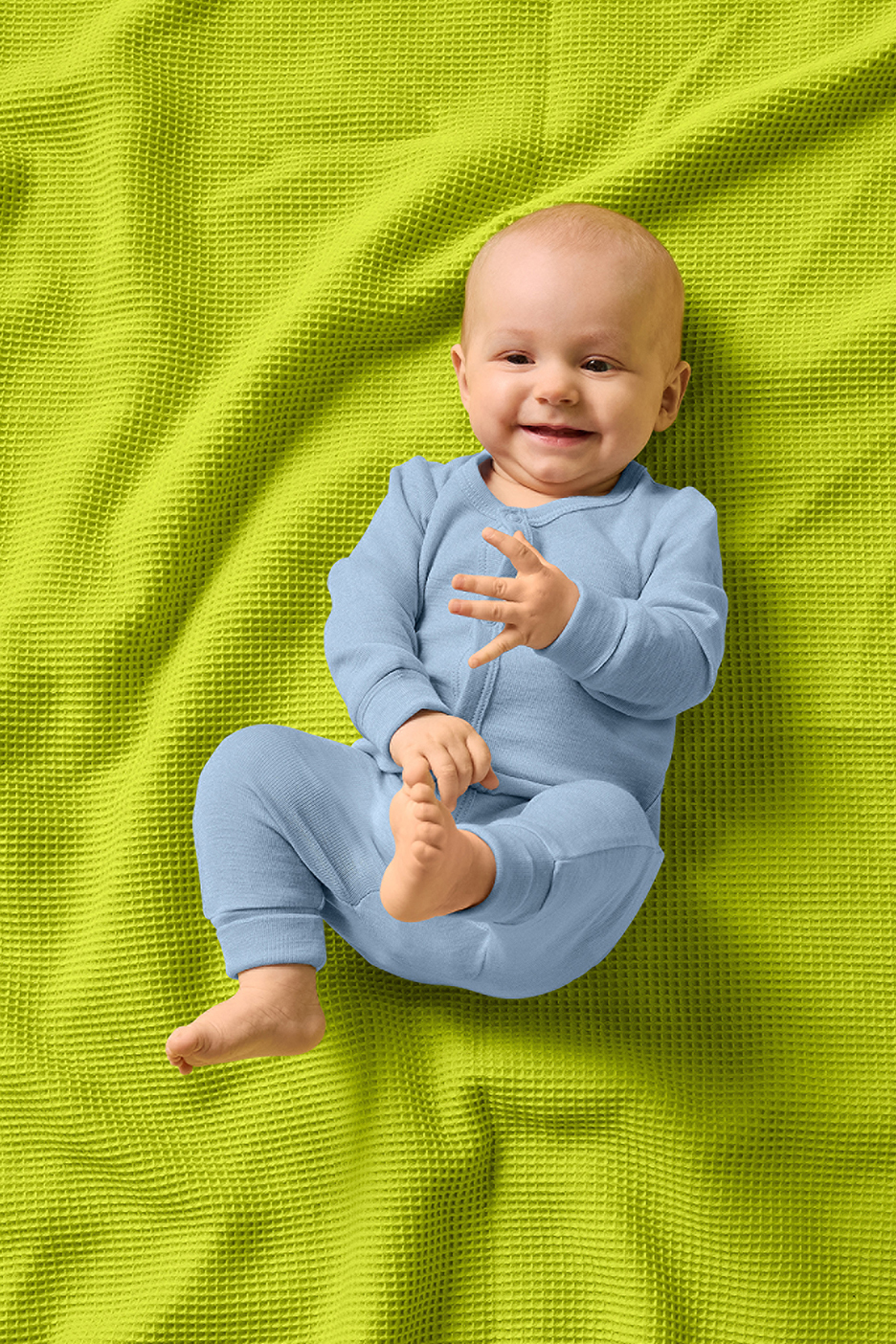 Naeratav beebi sinises kombinesoonis lamab erkrohelisel vahvlitekil.