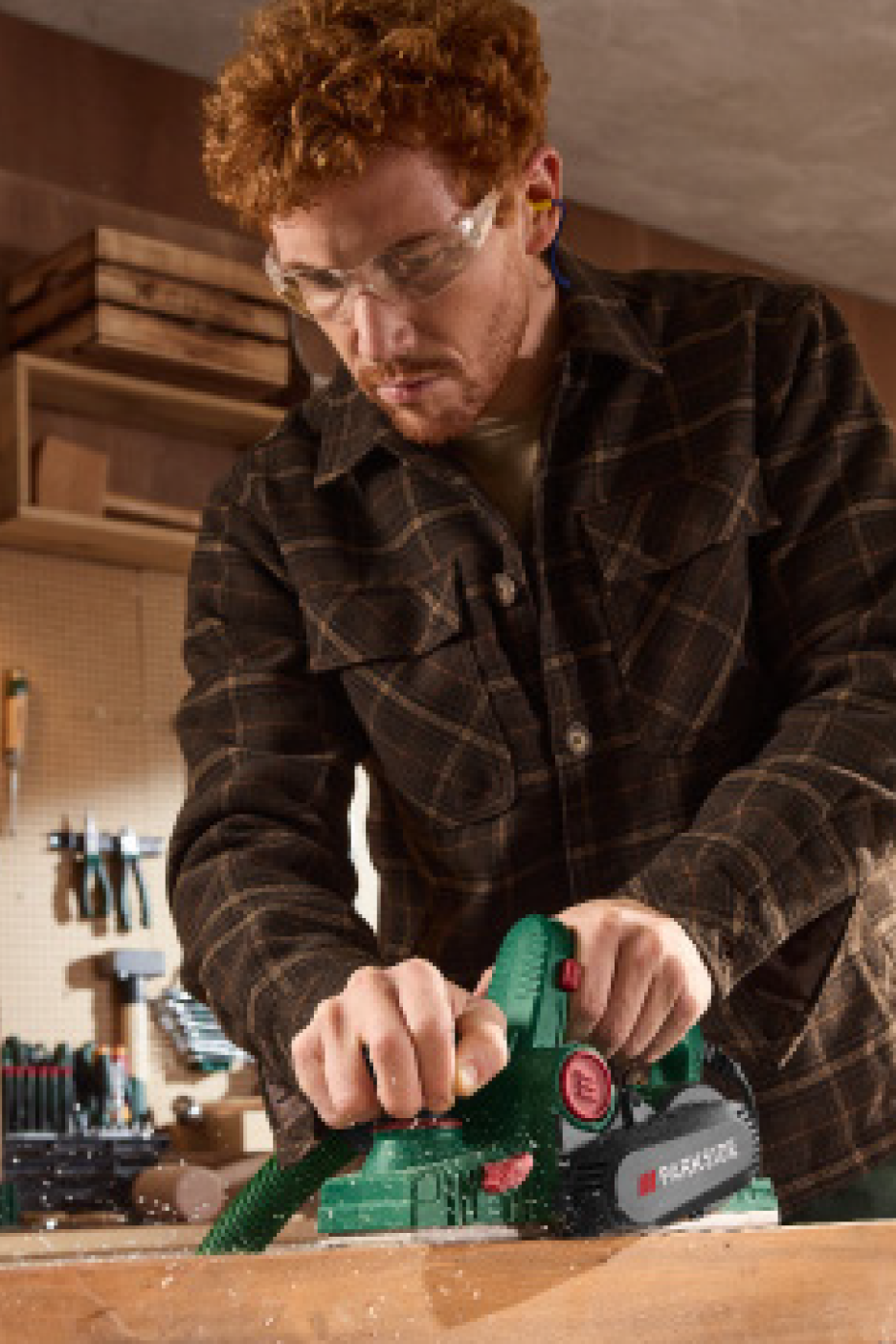 Kaitseprillide ja kõrvaklappidega mees hööveldab puidust lauda elektrilise höövliga.