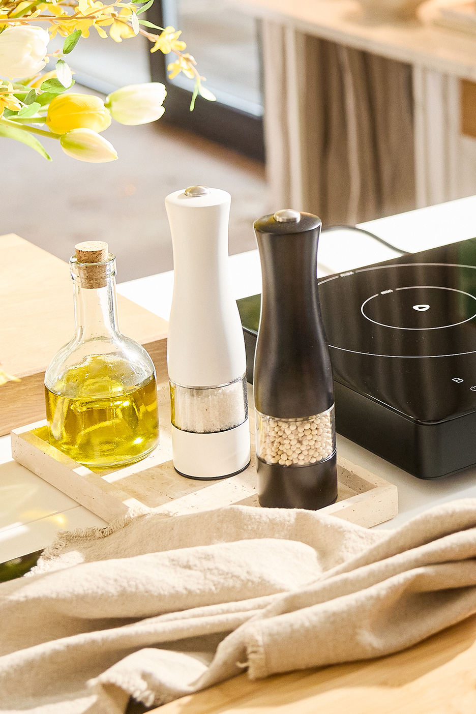 Õli, soola- ja pipraveskid köögilaual koos lillede ja linase rätikuga.