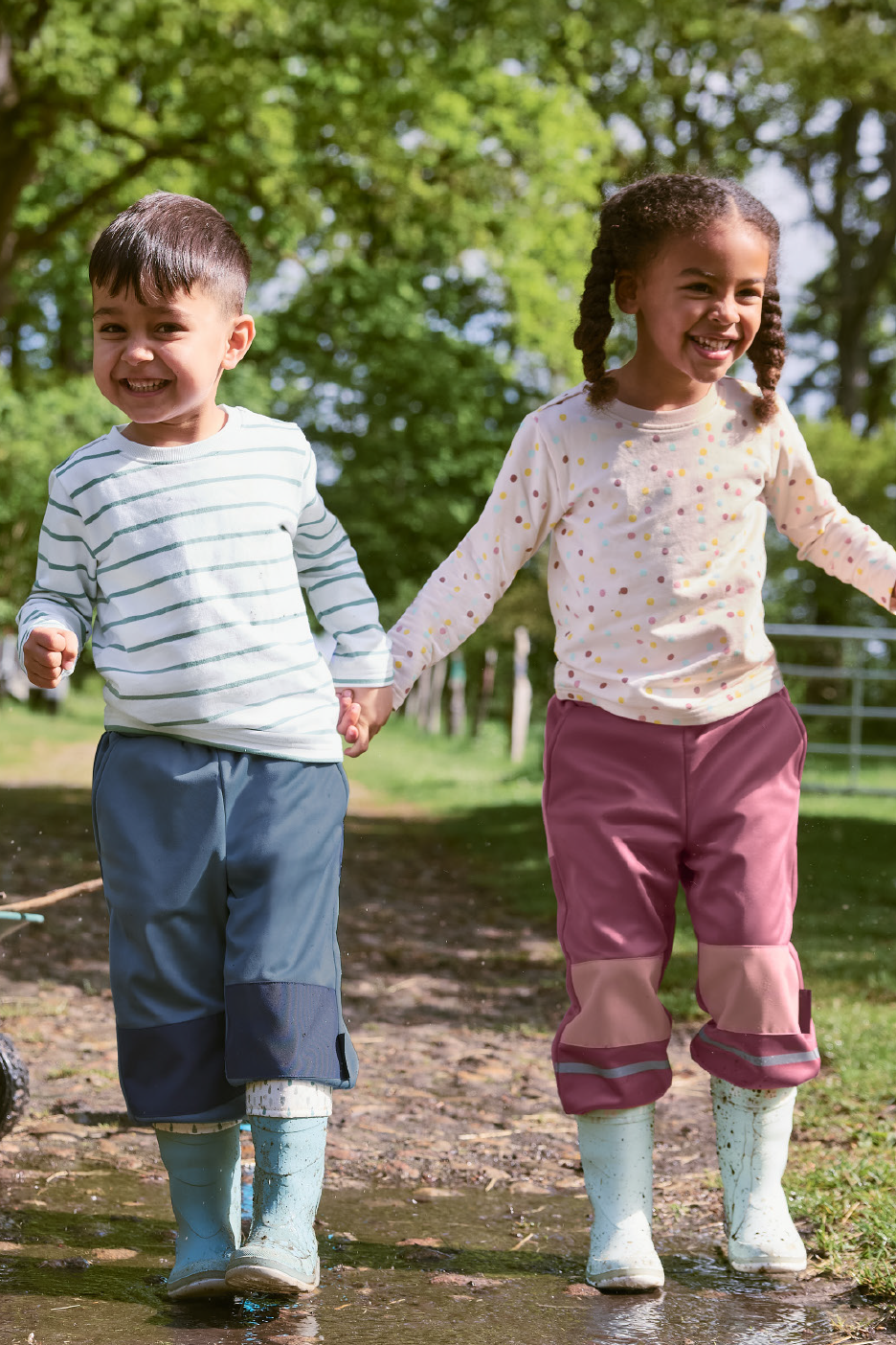 Kaks last veekindlates pükstes ja kummikutes hoiavad käest kinni ja naeratavad.