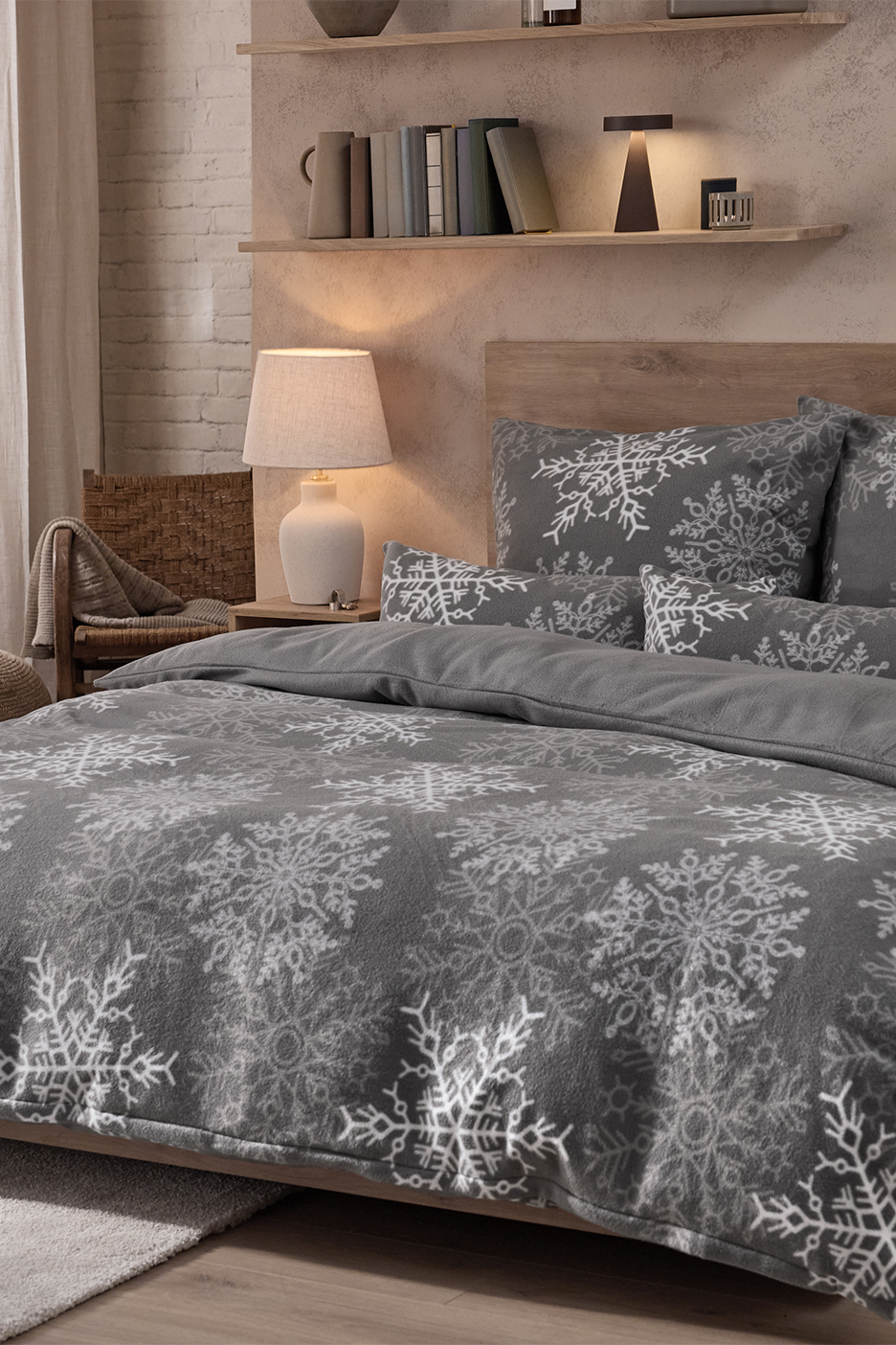 Hall voodipesu valgete lumehelvestega magamistoas, puidust riiulite ja lambiga.