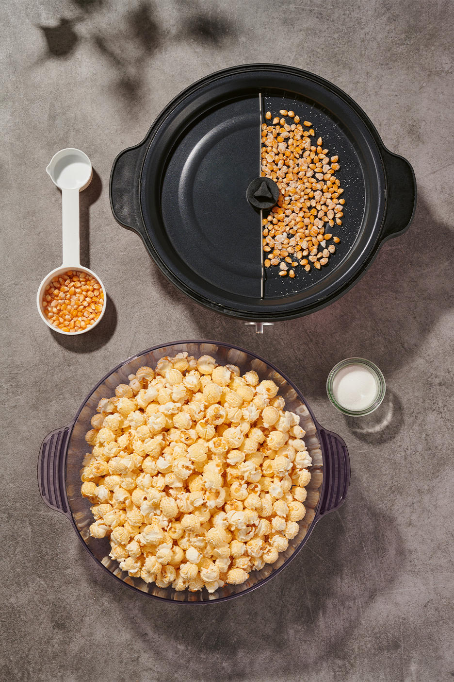 Popkornimasin, mõõtelusikas maisiteradega, kauss popkorniga ja soolaga