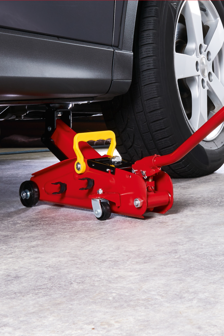 Punane hüdrauliline tungraud halli auto all betoonpõrandal.