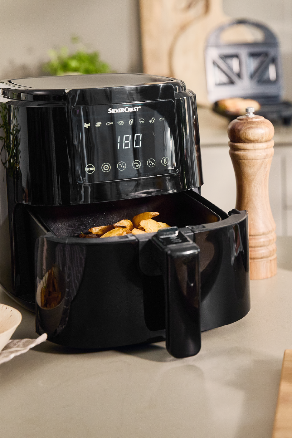 Must õhkfritüür krõbedate kartulitega köögis, taustal puidust pipraveski.