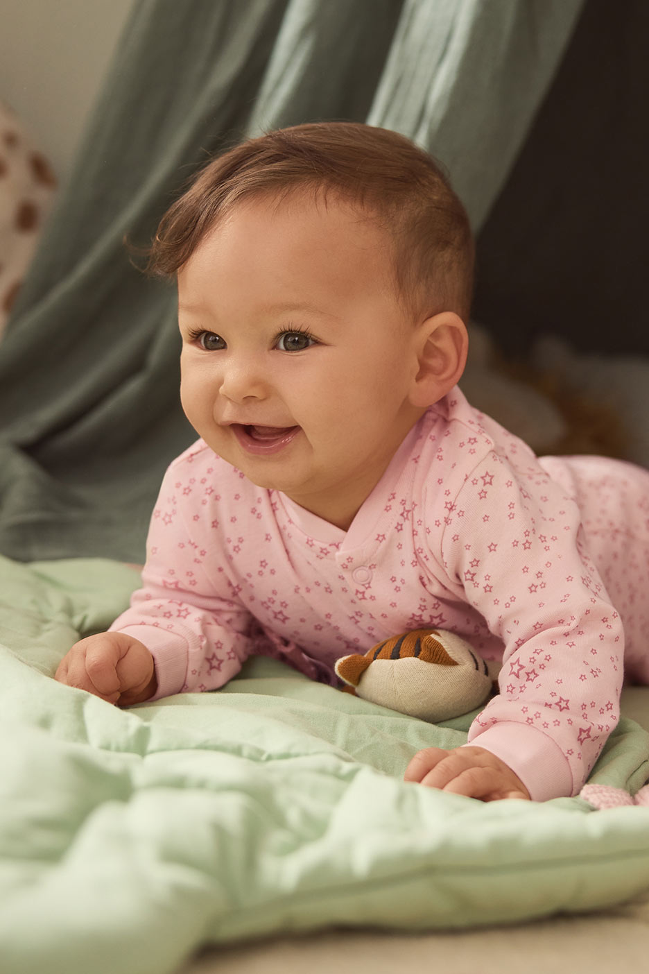 Naeratav beebi roosas tärnimustriga kombinesoonis lamab rohelisel tekil.