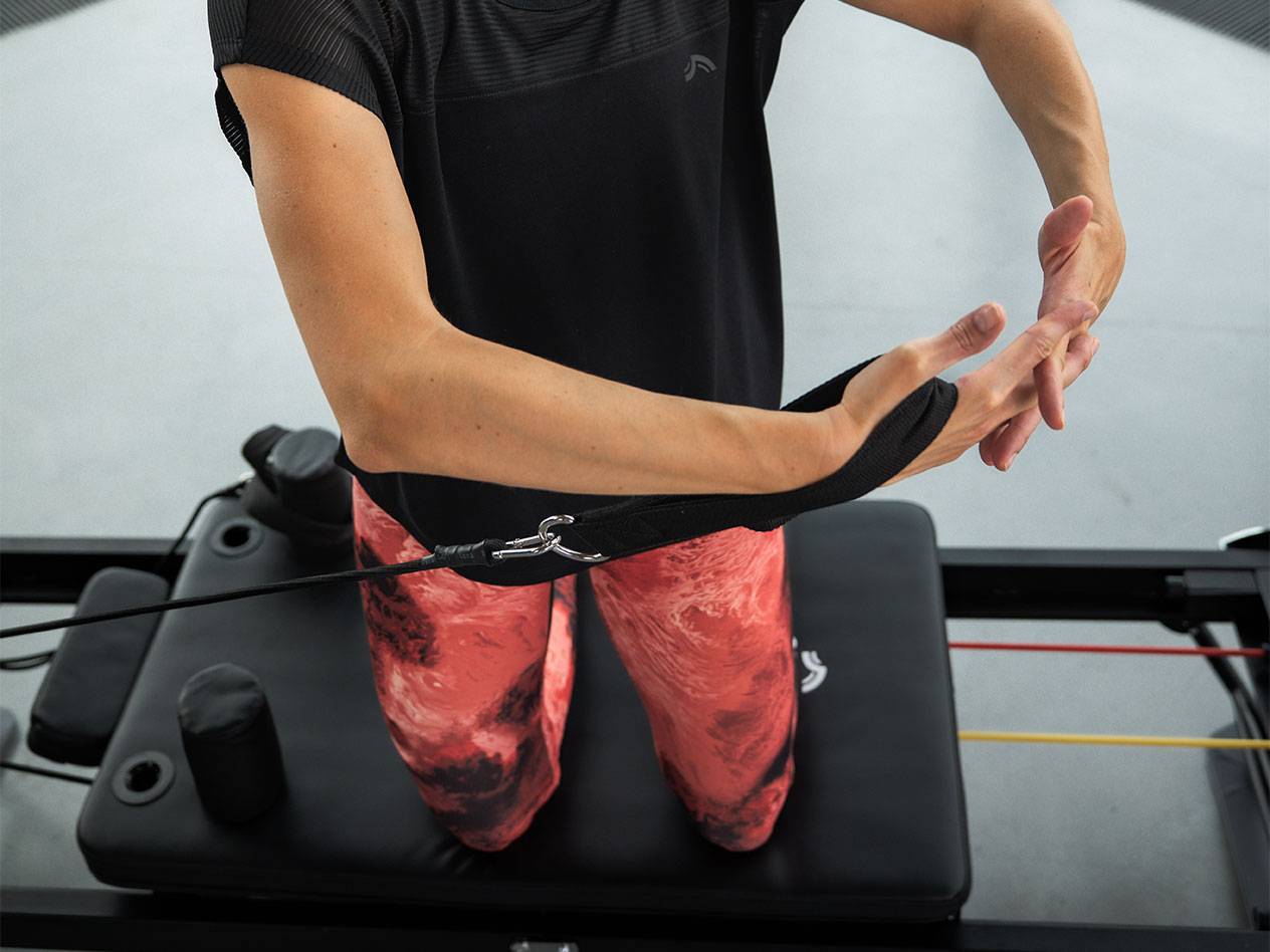 Женщина тренируется с эспандерами на тренажере для пилатеса.