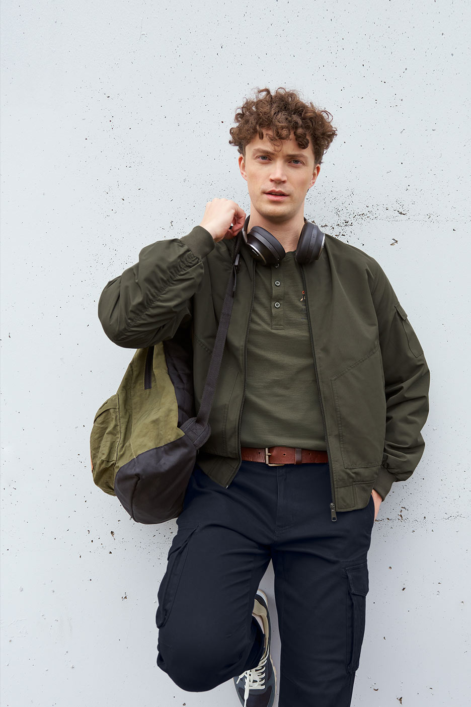 Mees rohelises pommitajakostüümis, rohelises T-särgis, mustades cargo pükstes ja kõrvaklappides.