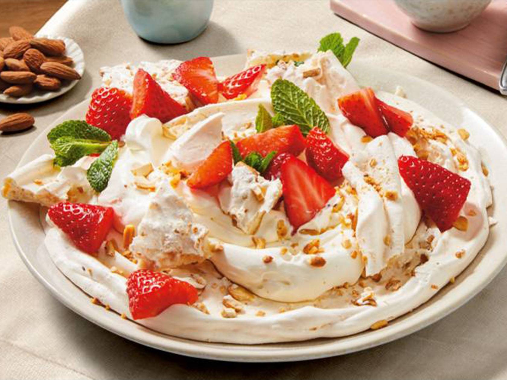 Pavlova maasikate ja mandlitega valgel taldrikul.
