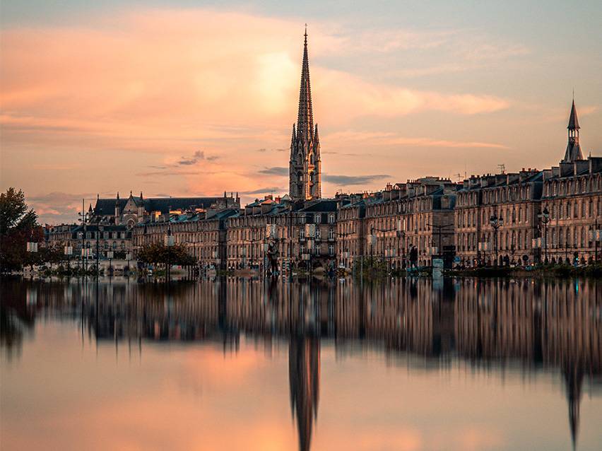 Bordeaux' linna siluett päikeseloojangul kiriku ja selle peegeldusega vees.