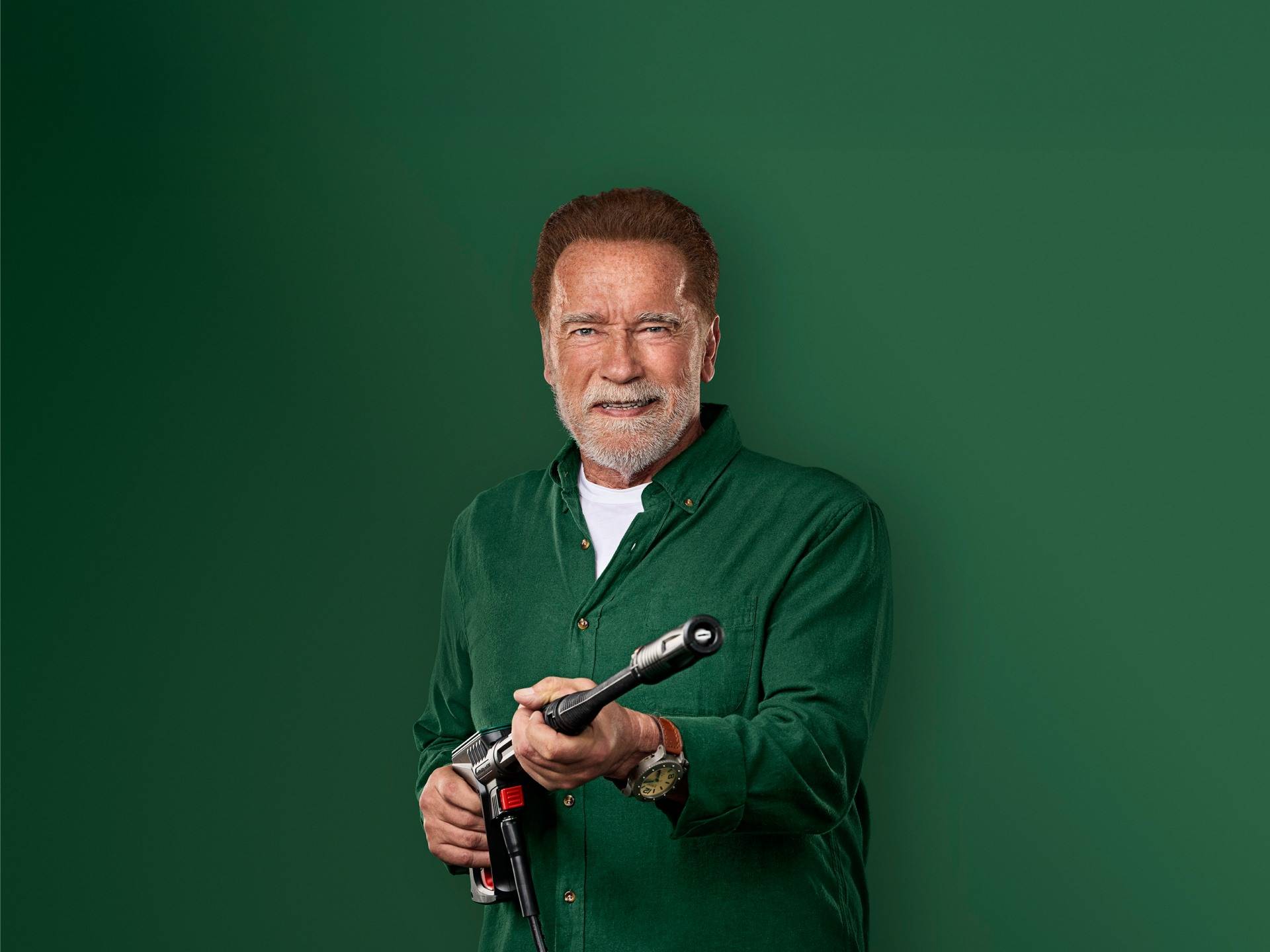 Arnold Schwarzenegger naeratab, hoides survepesuri püstolit.