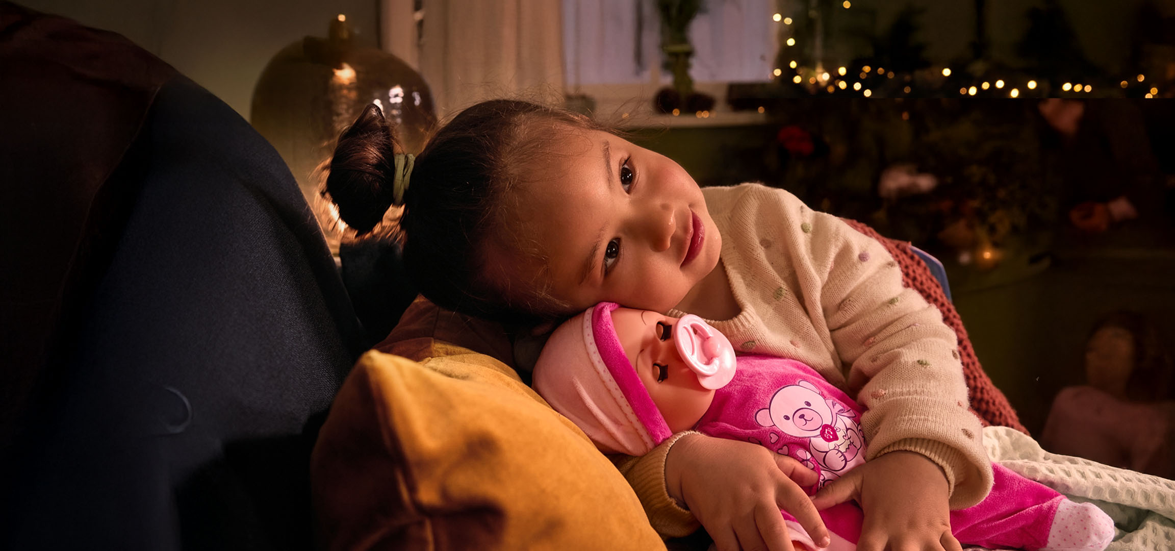 Девочка с куклой и соской, уютно устроившаяся на подушке.