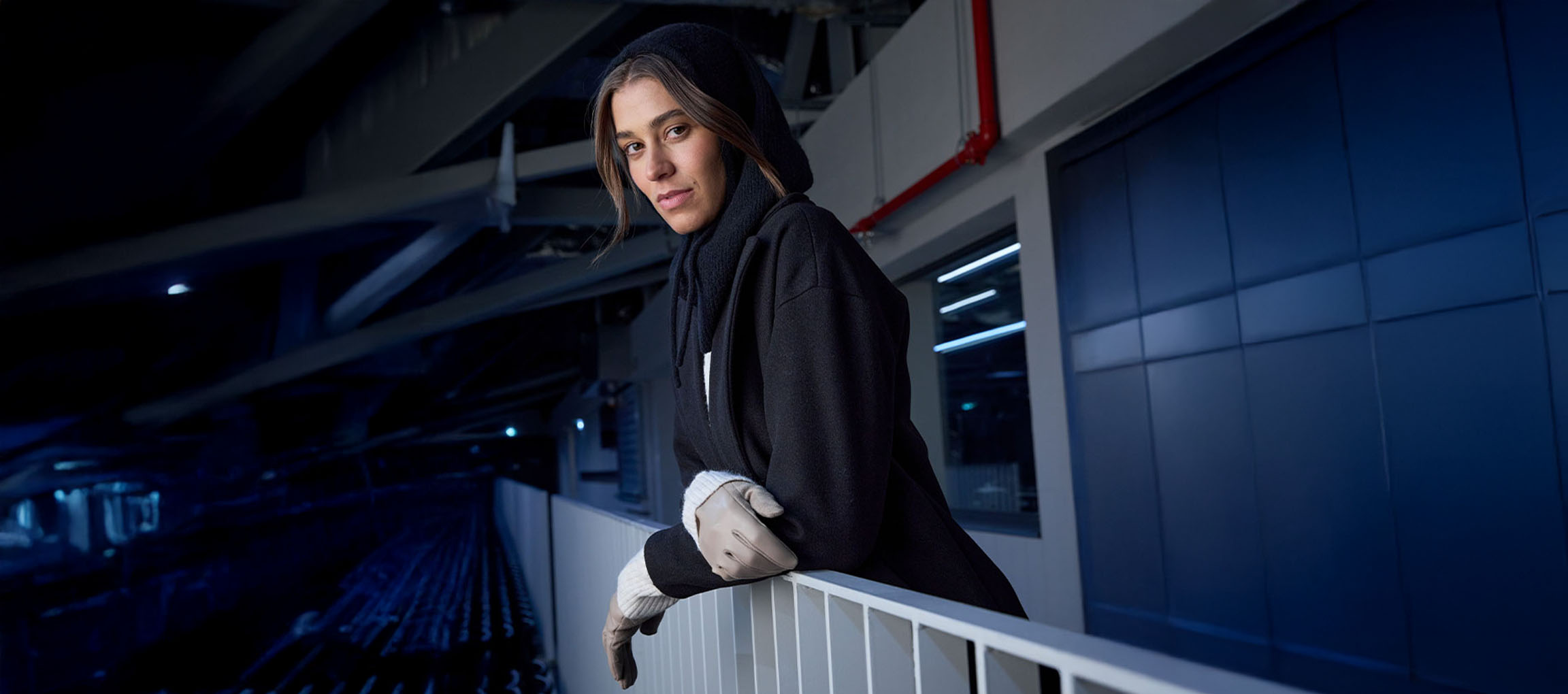 Naine mustas mantlis ja kinnastes toetub linnakeskkonnas piirdele.