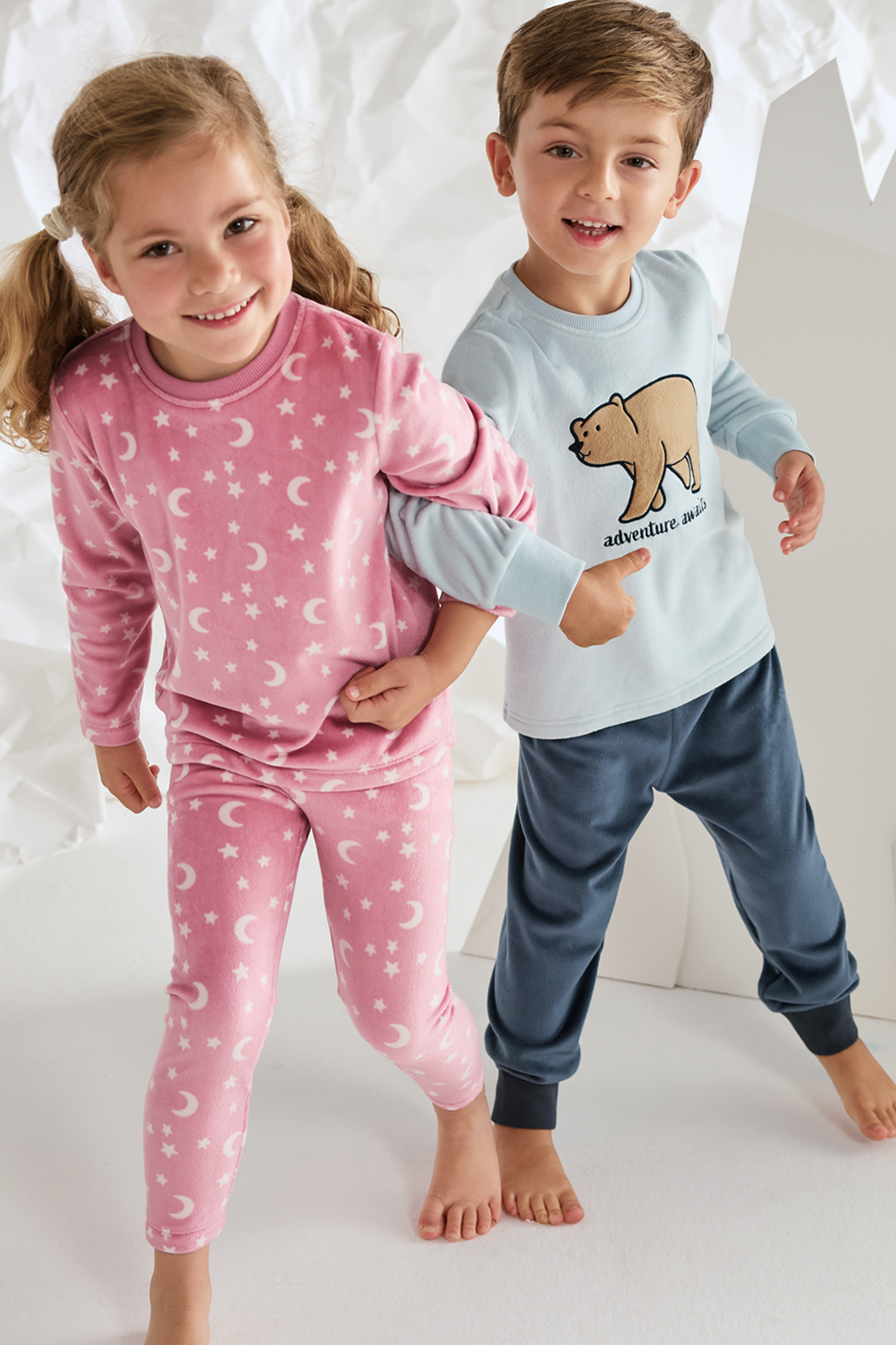 Lapsed kannavad roosasid ja helesiniseid pidžaamasid, millel on kuu, tähed ja karu.