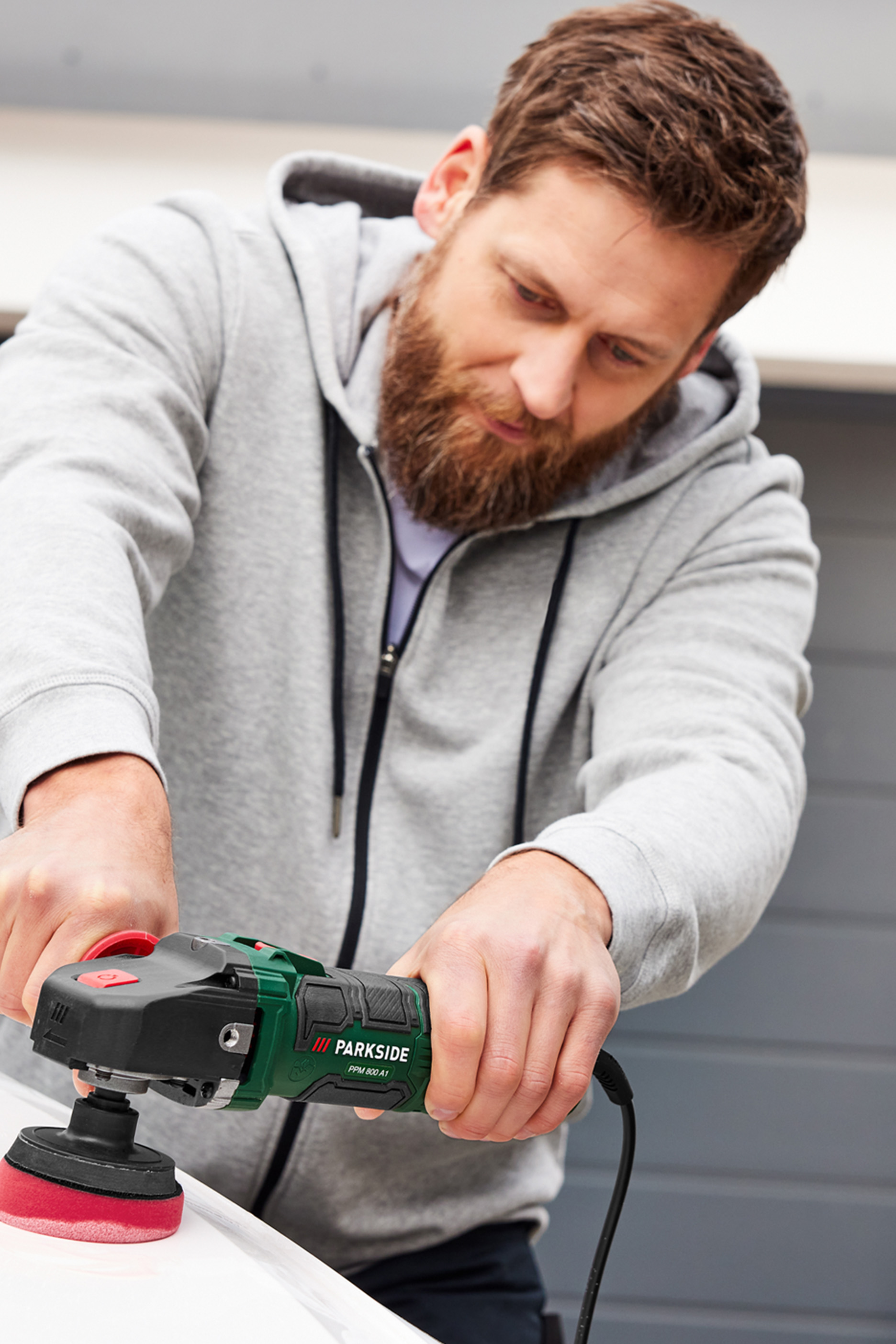 Hallis dressipluusis mees poleerib pinda Parkside poleerimismasinaga.