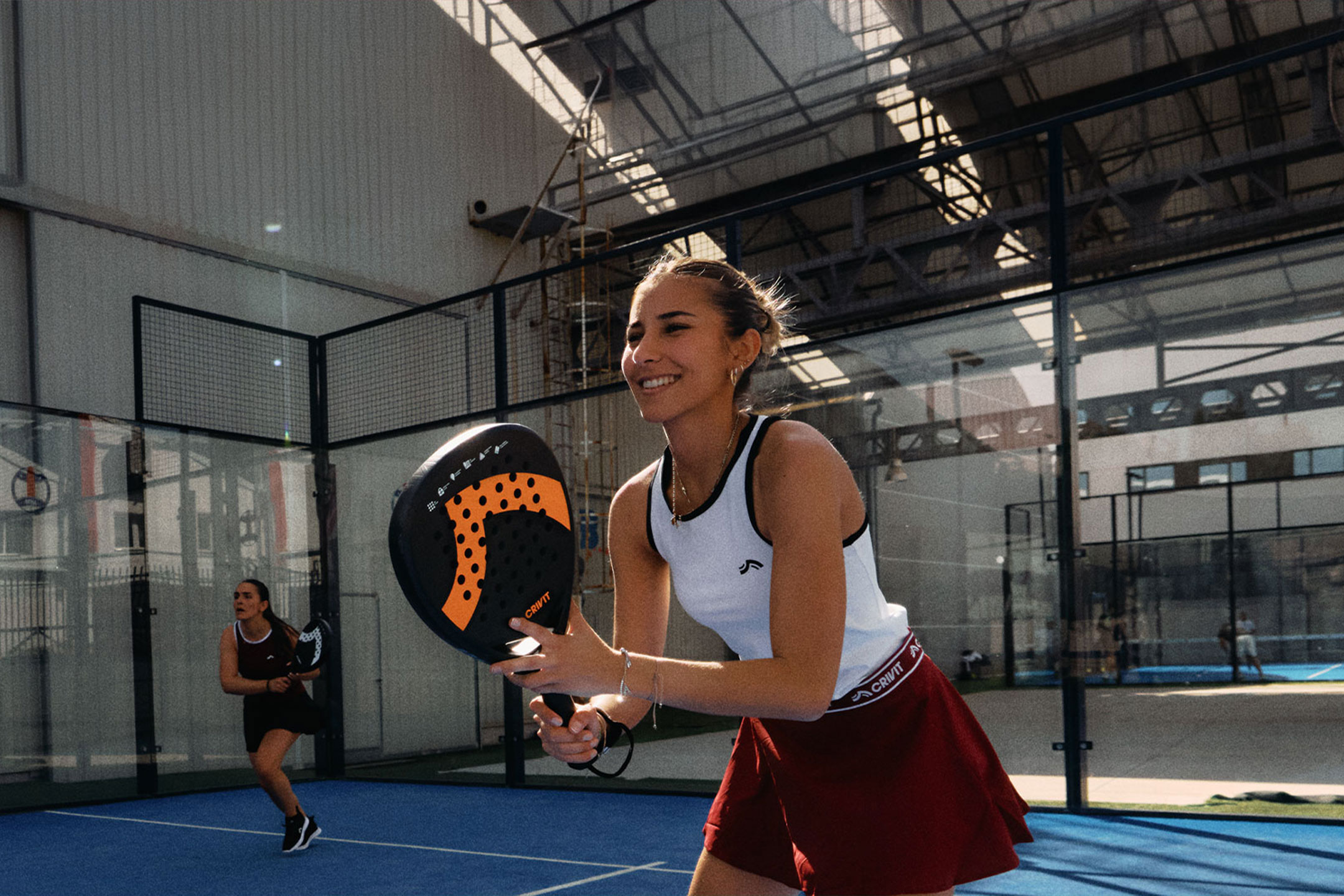 Tehisintellekti loodud: Kaks naist mängivad padelit, üks naeratab ja hoiab reketit, sinisel väljakul.