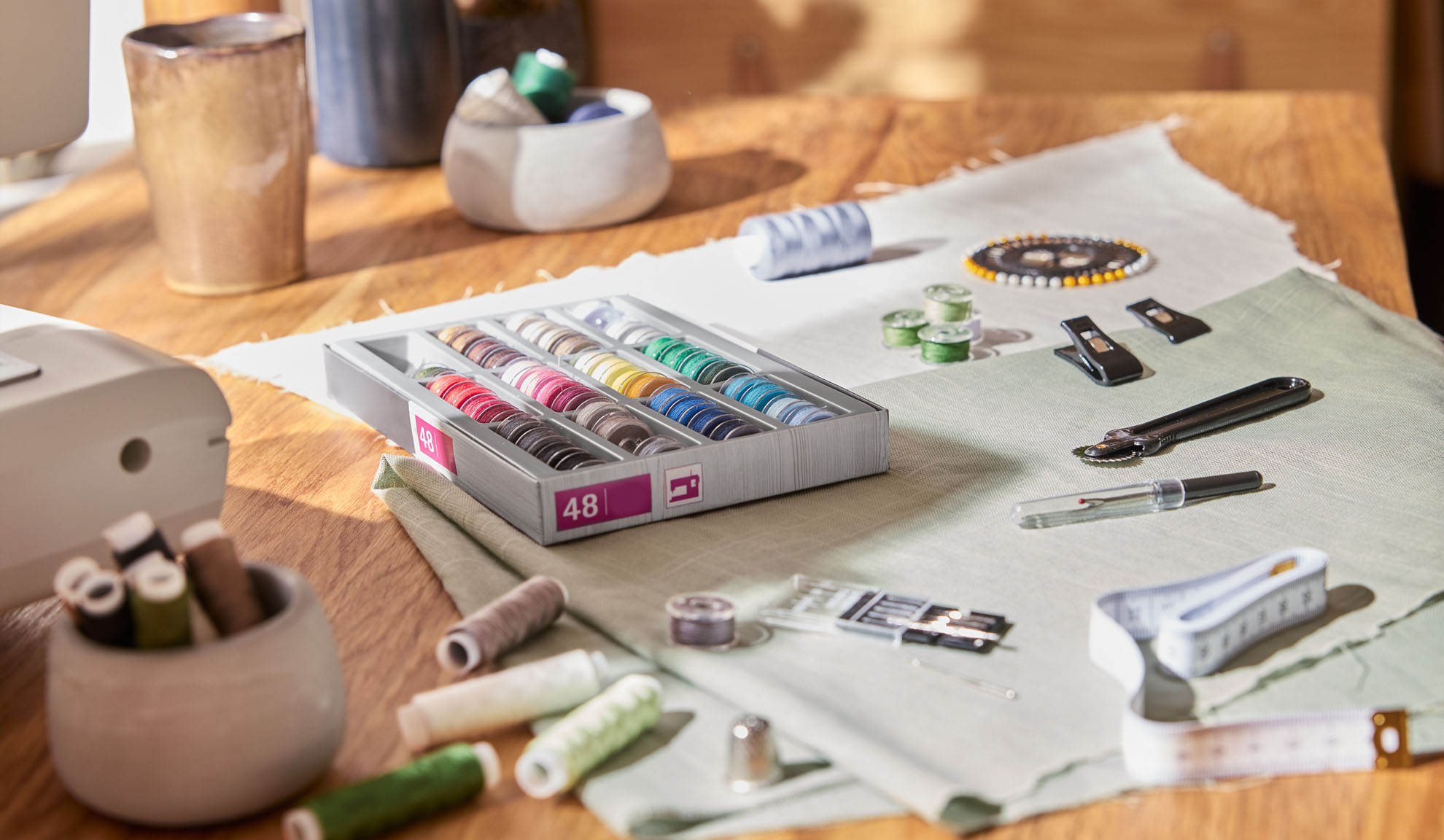 Õmbluskomplekt värviliste niitide karbi, õmblusmasina ja tööriistadega puidust laual.