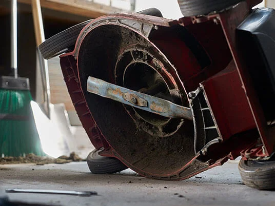 Грязная газонокосилка вверх дном, видно лезвие