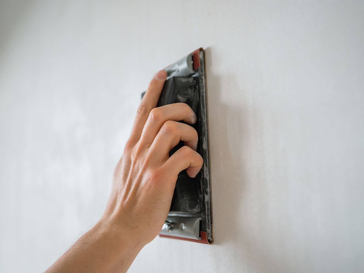 Käsi lihvib seina lihvimisklotsiga