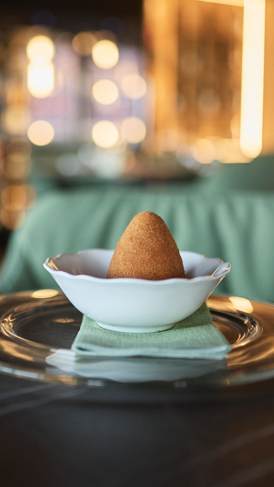 Kuldne arancini valges kausis rohelisel salvrätikul ja klaasplaadil.