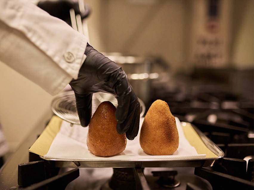 Mustade kinnastega kokk asetab praetud arancini paberrätikutega alusele.
