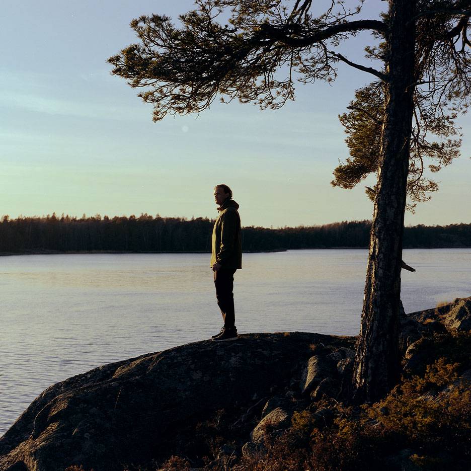 Matkajakiga mees järve ääres, puu esiplaanil.