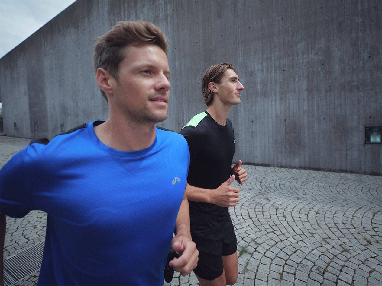 Kaks meest jooksevad spordisärkides ja lühikestes pükstes, üks sinises ja teine mustas.