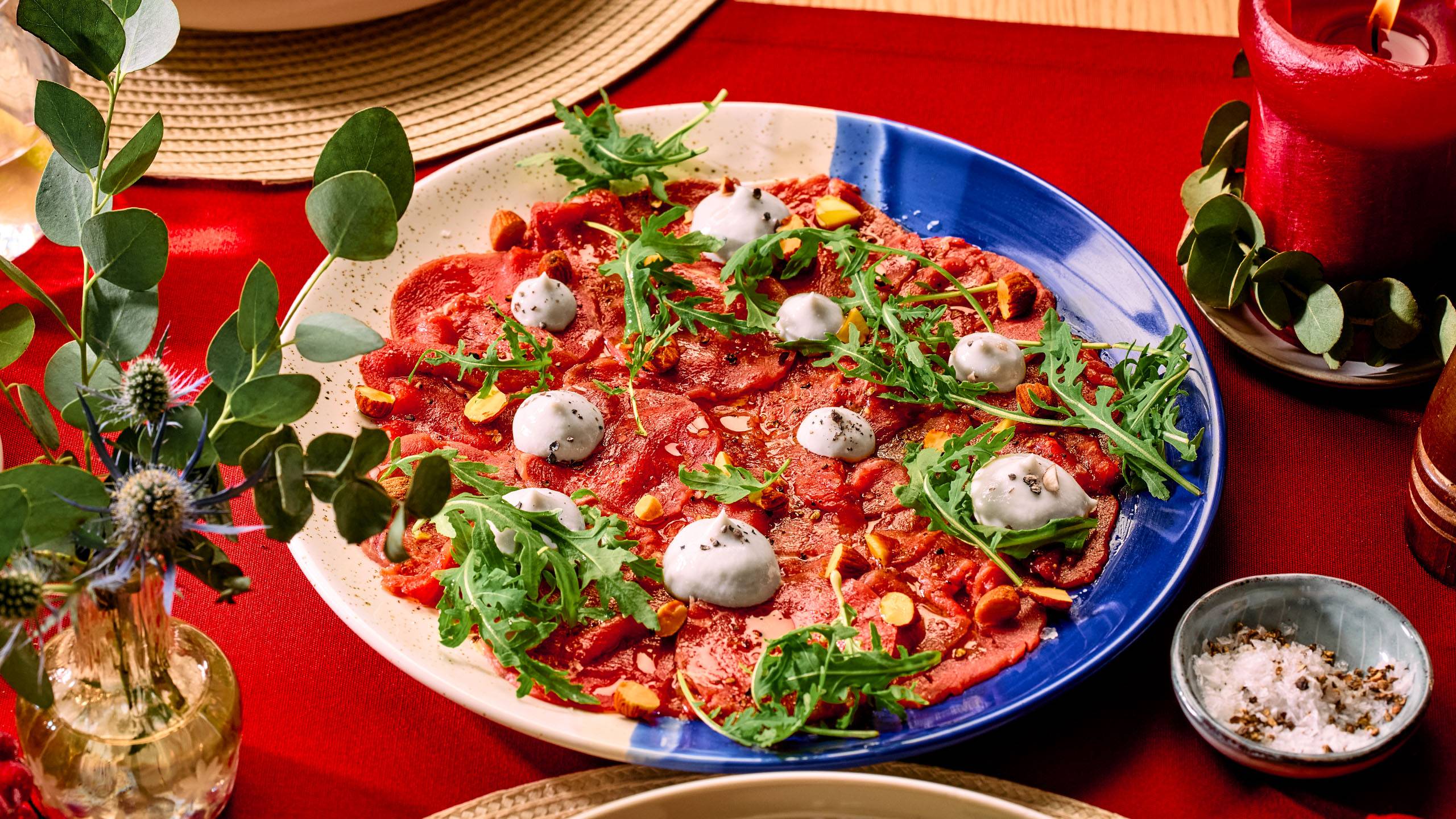 Carpaccio roheliste ja valgete kreemilaikudega sinisel ja valgel taldrikul, punasel laual