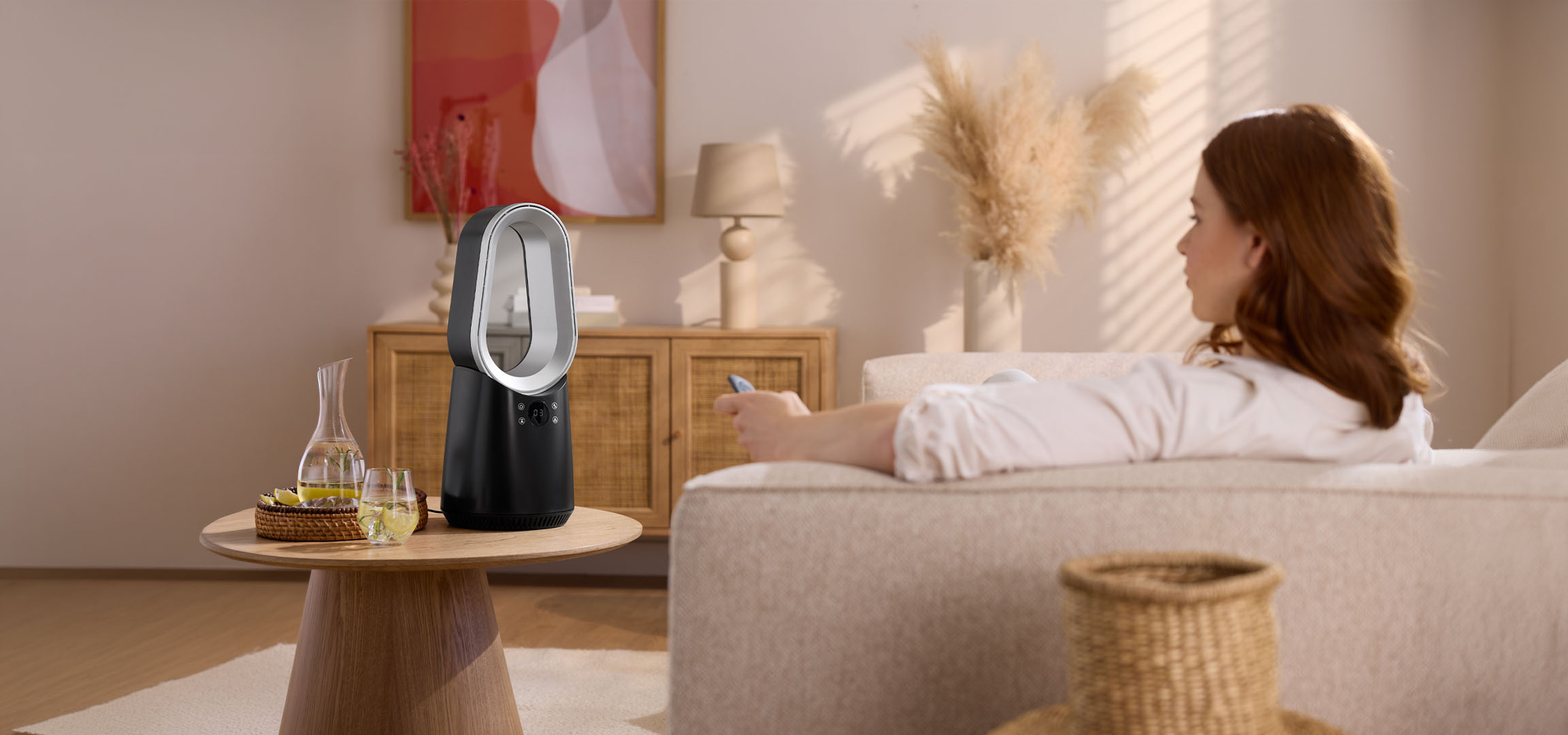 Naine diivanil puldiga, kaasaegne ventilaator ja joogid laual.