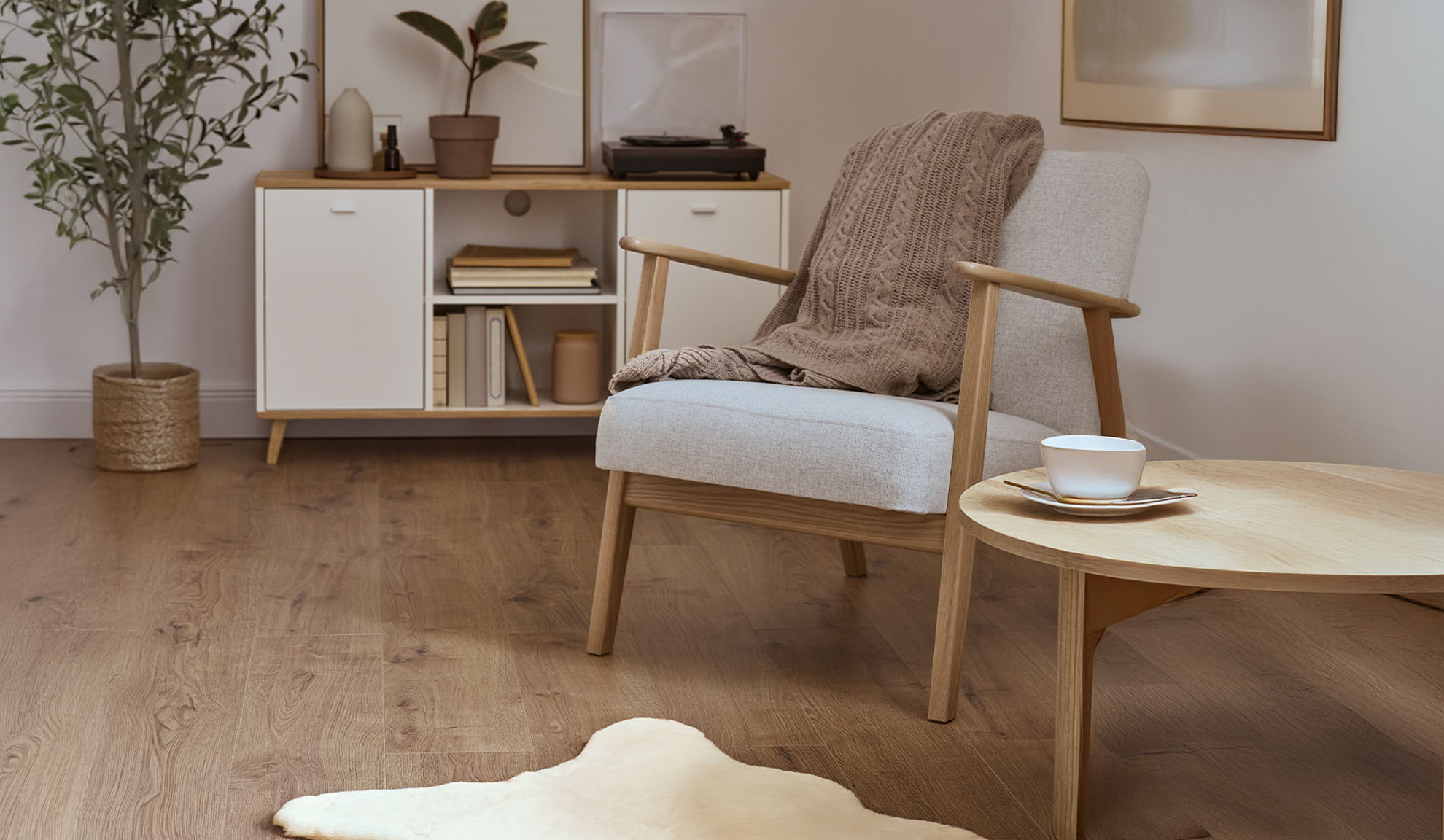 Уютное кресло с пледом, деревянный журнальный столик и шкаф для хранения в светлой гостиной.