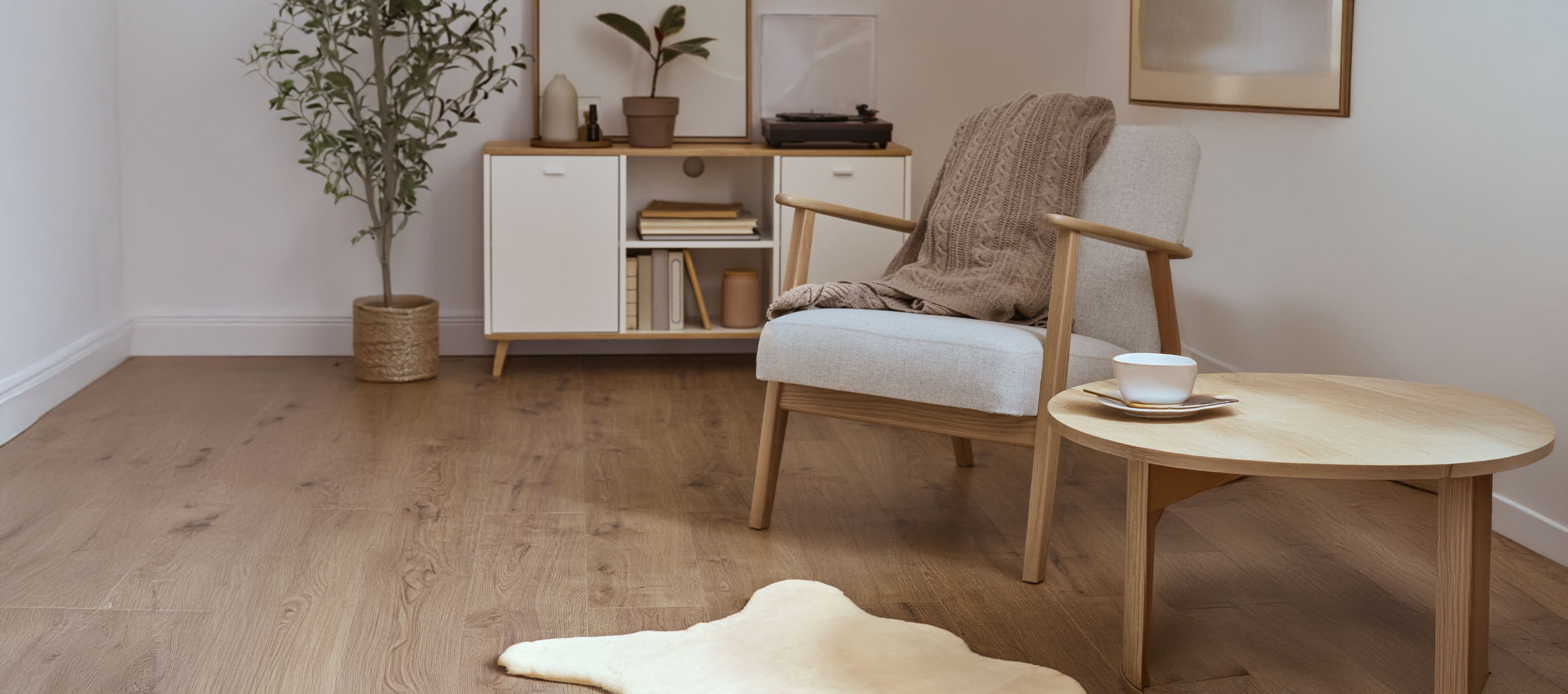 Серое тканевое кресло с вязаным пледом, деревянный кофейный столик и современный буфет.