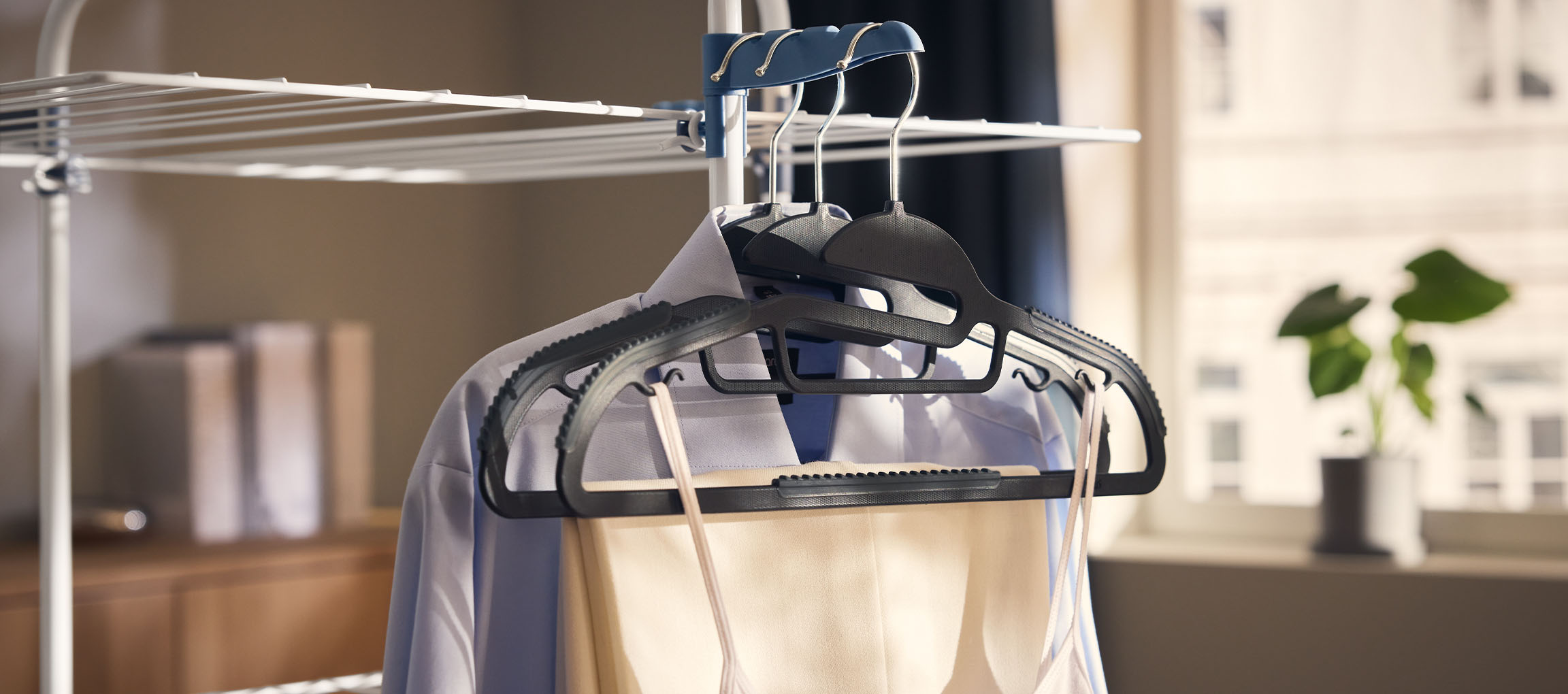 Одежда на вешалках на сушилке, с растением на заднем плане.