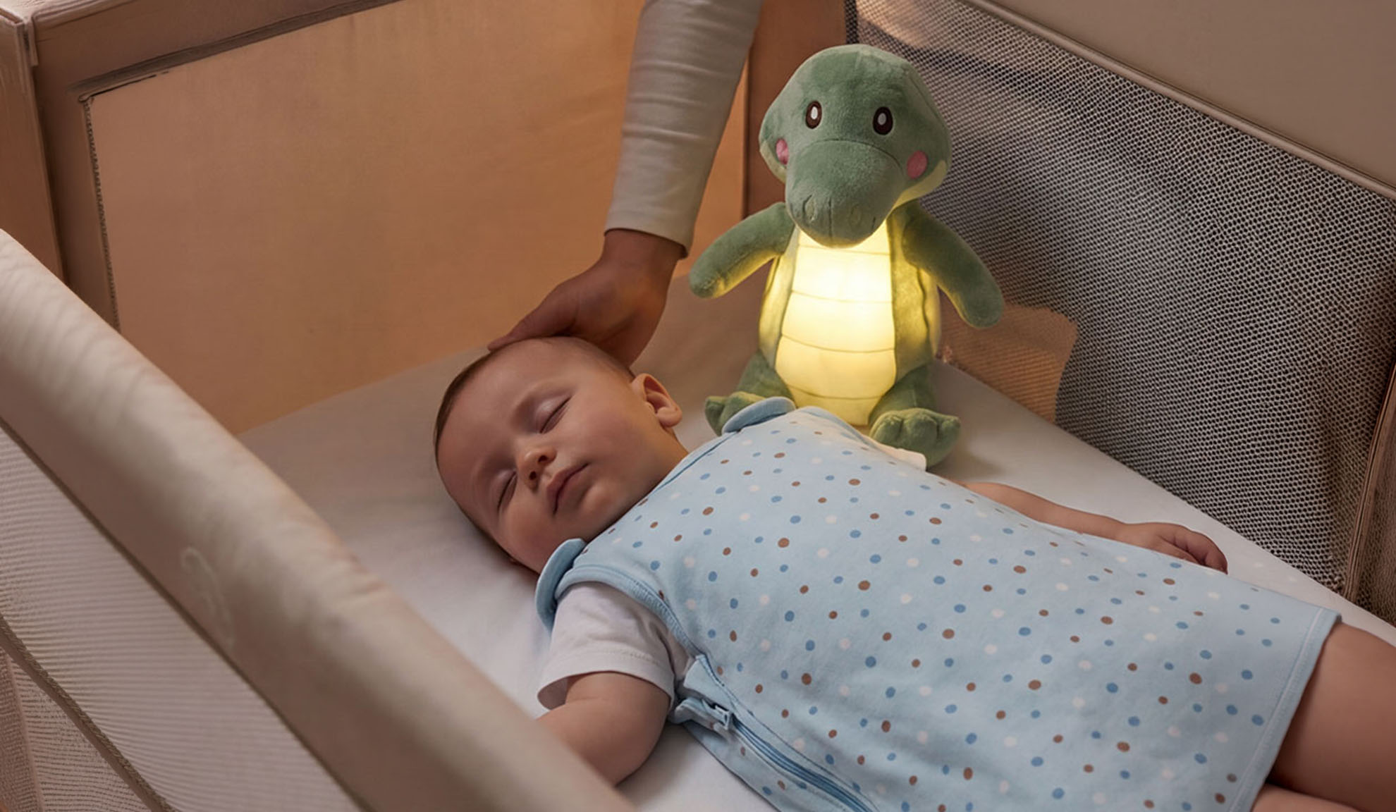 Beebi magab võrevoodis pehme mänguasja ja vanema käega.