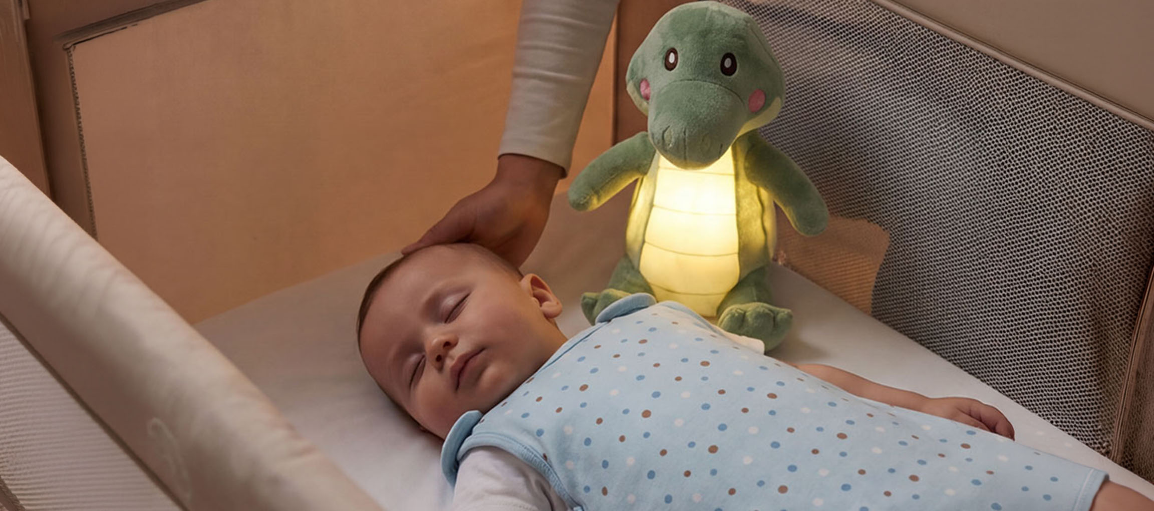 Beebi magab võrevoodis plüüšist öölambiga, täiskasvanu silitab beebi pead.