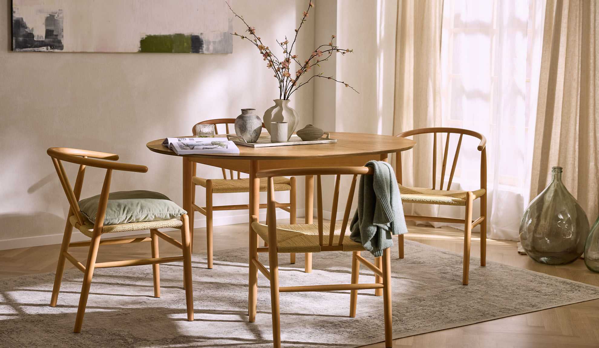 Valgusküllane söögituba ümmarguse puidust laua, nöörist istmetega puidust toolide ja lilledekoratsiooniga.