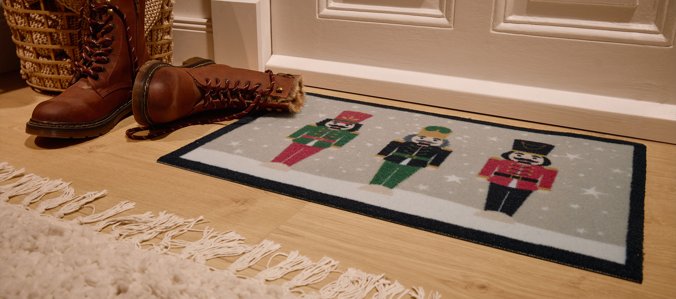 Jõuluteemaline uksematt pähklipurejatega, pruunid saapad ja vitstest korv sissepääsu juures.