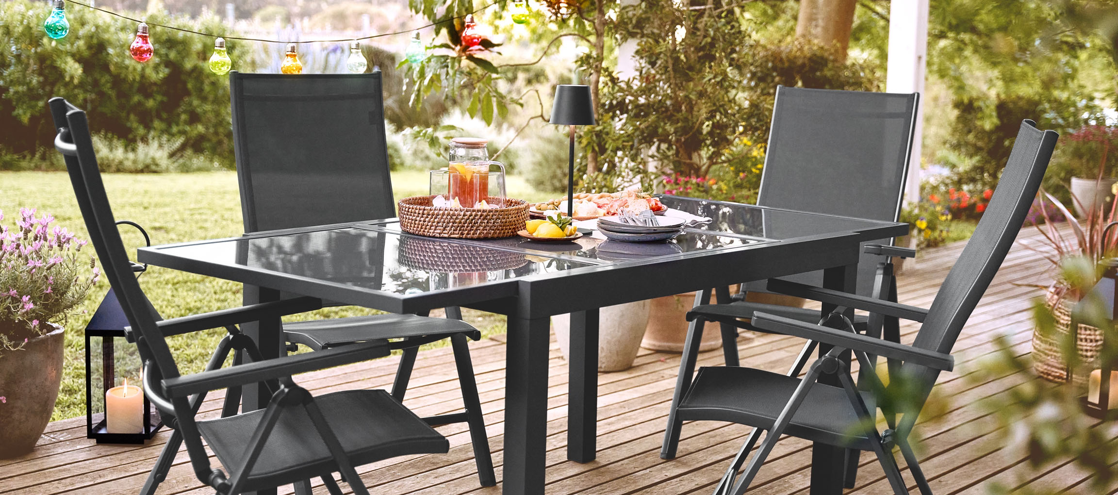 Conjunto de móveis de jardim em metal cinza-escuro com cadeiras dobráveis e mesa de vidro.