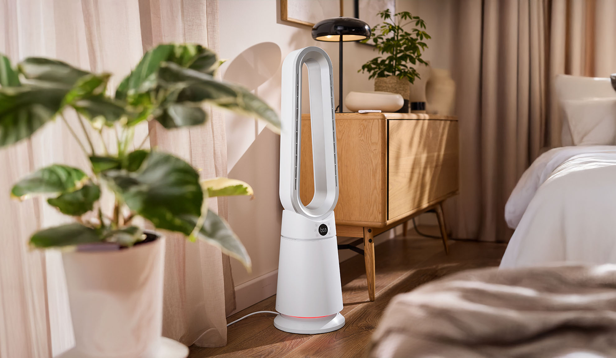 Valge tornventilaator kaasaegses magamistoas taimede ja puitmööbliga.