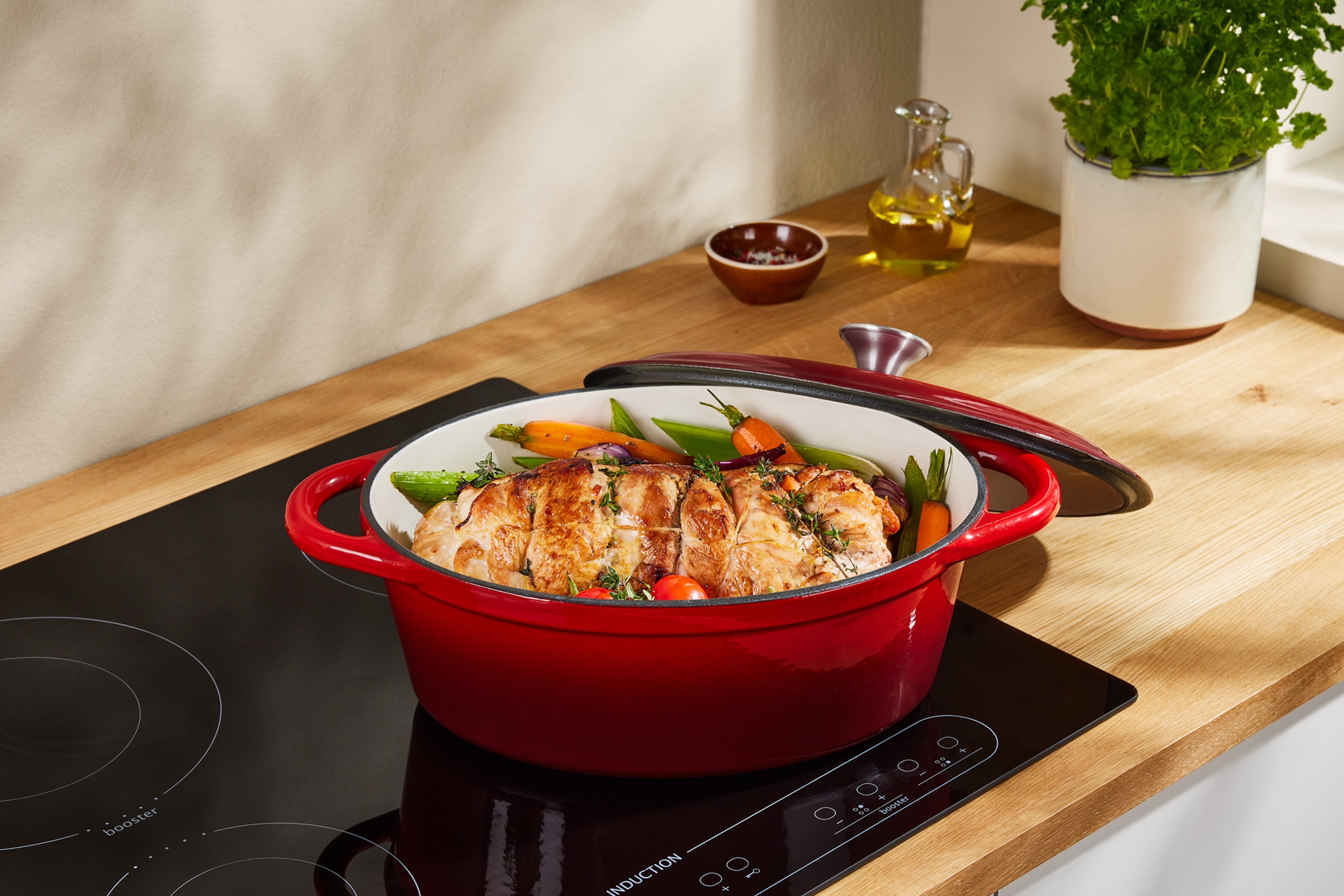 Красная чугунная кастрюля с жареным мясом и овощами на индукционной плите