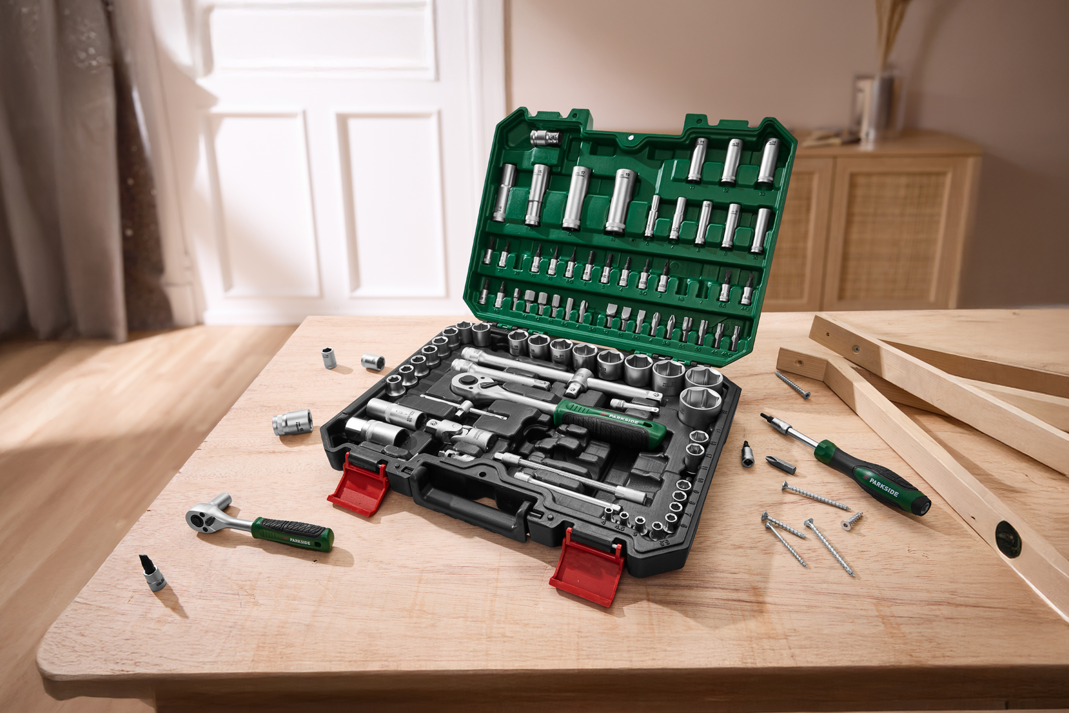 Набор инструментов PARKSIDE в зеленом кейсе на деревянном столе, рядом шурупы и деревянные бруски.