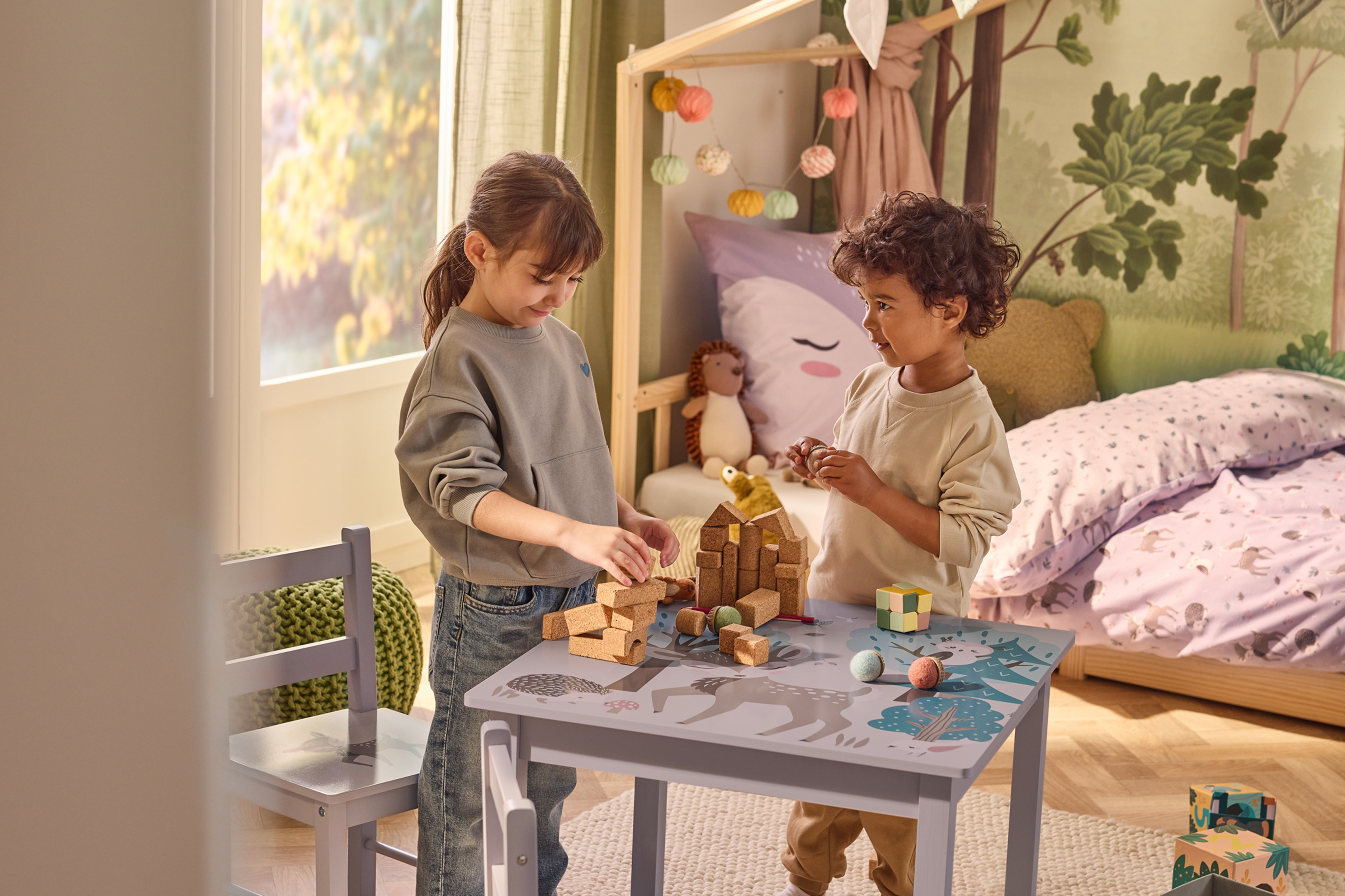 Двое детей играют с деревянными кубиками за детским столом в спальне.