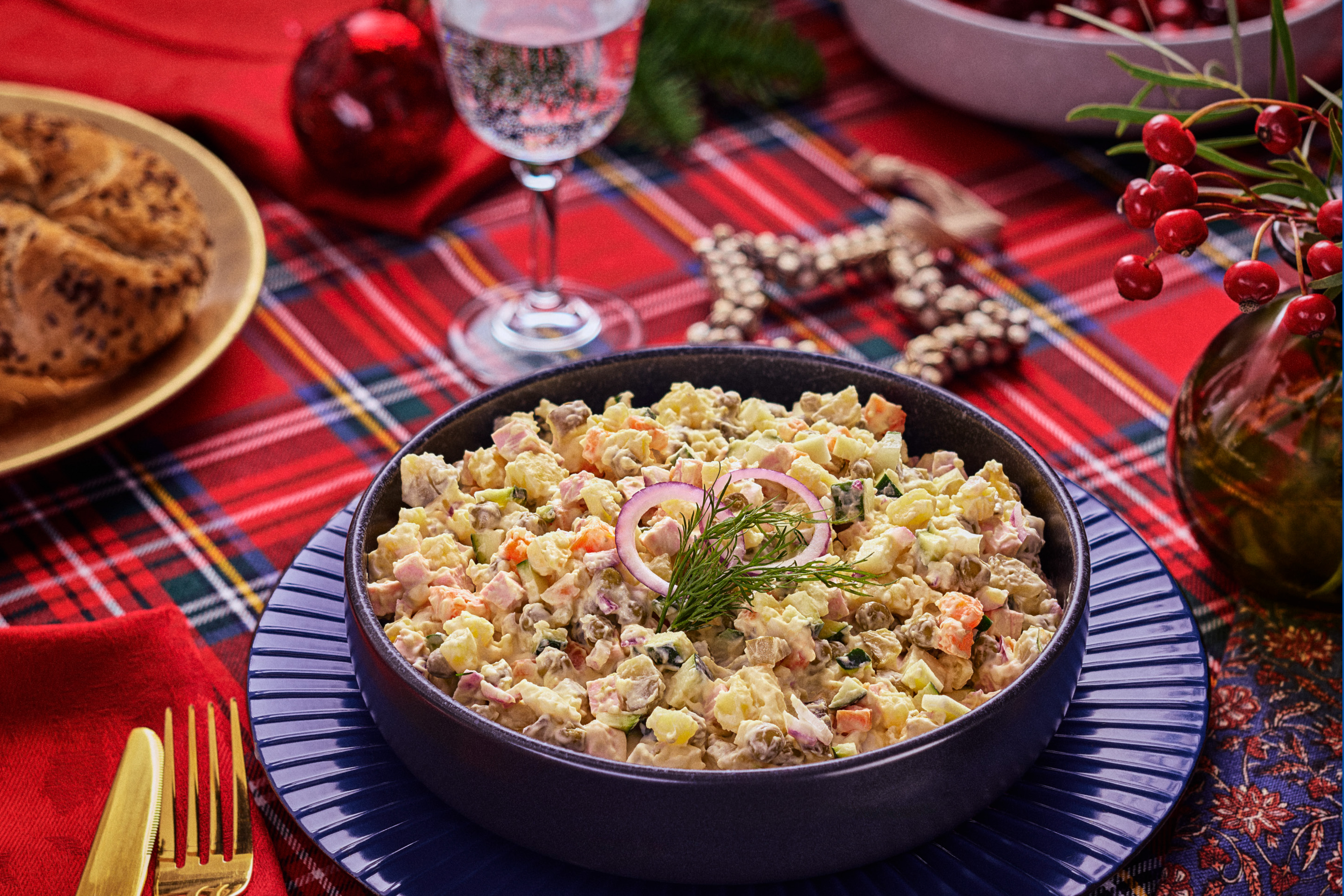 Olivier' salat mustas kausis sinisel taldrikul, punase ruudulise laudlina taustal.